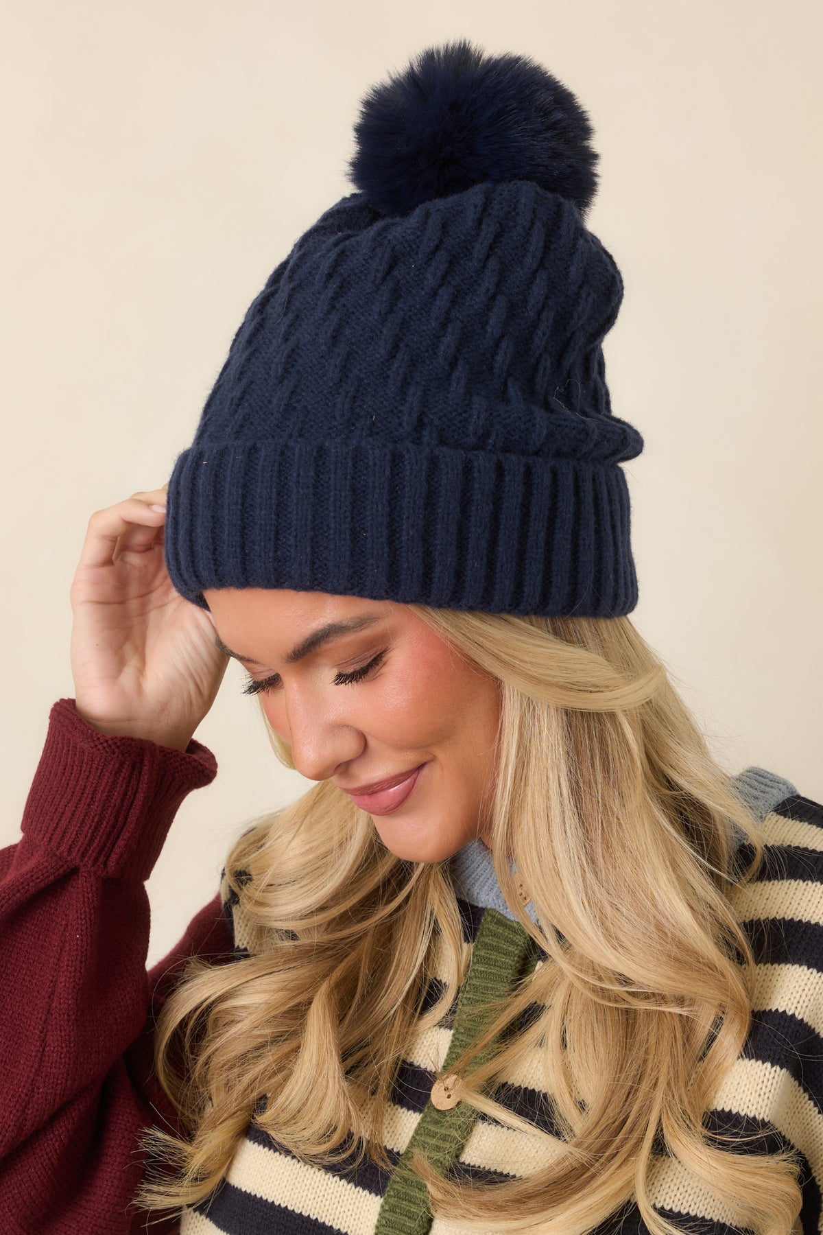 Knit hat features a classic cable pattern, fluffy tonal pom, wide fold-over ribbed cuff, and relaxed slouchy crown.