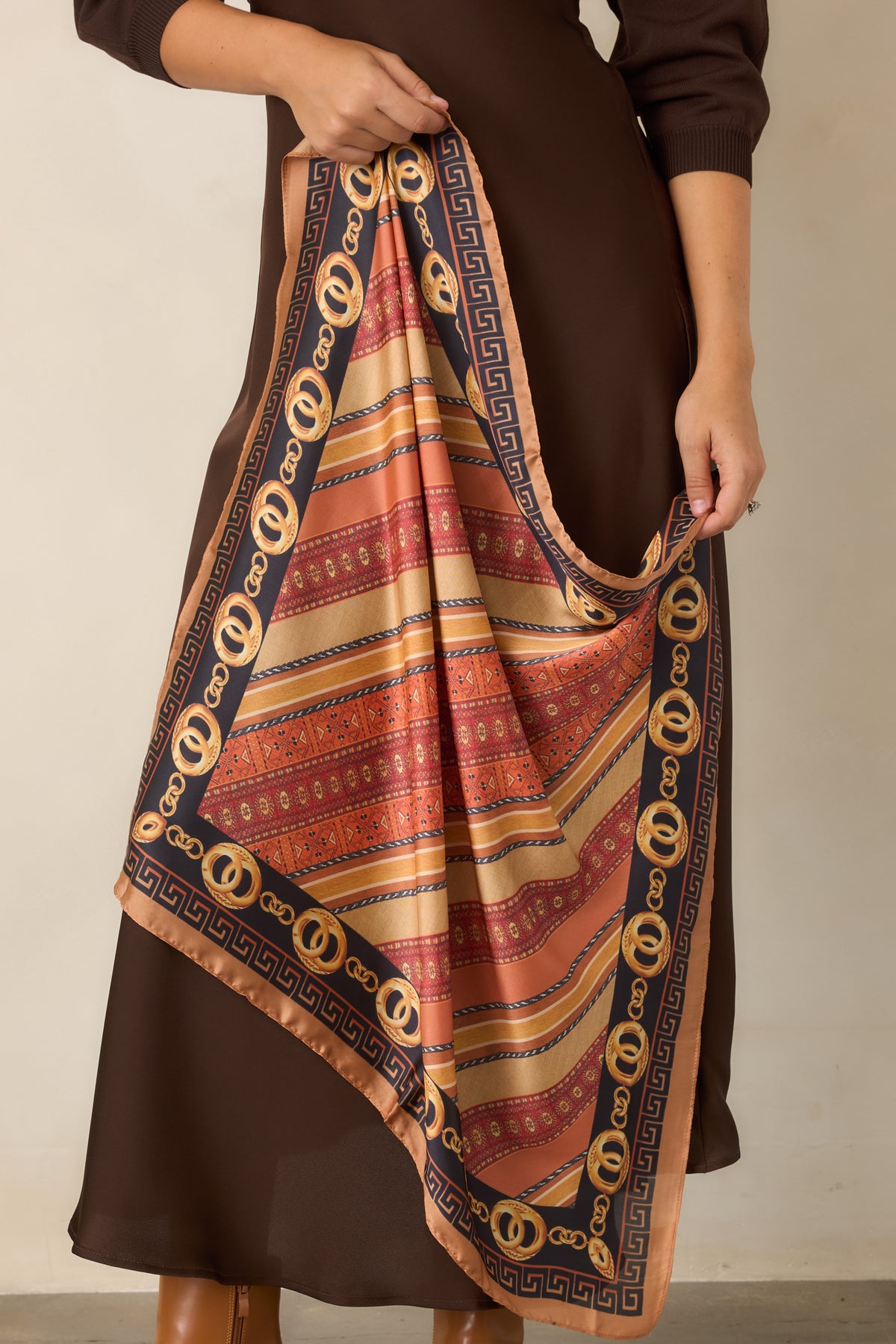 Square scarf highlighting patterned stripes framed by a Greek key border in camel and black with rust and burgundy accents.