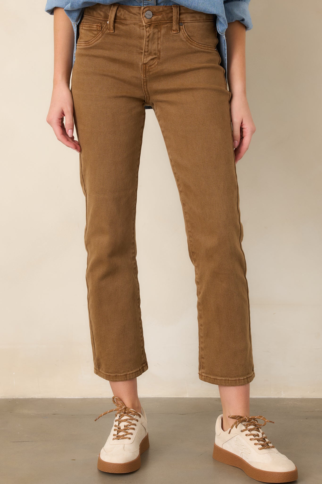 Camel brown pants highlighting the mid-rise waistband and classic five-pocket construction in structured cotton denim.