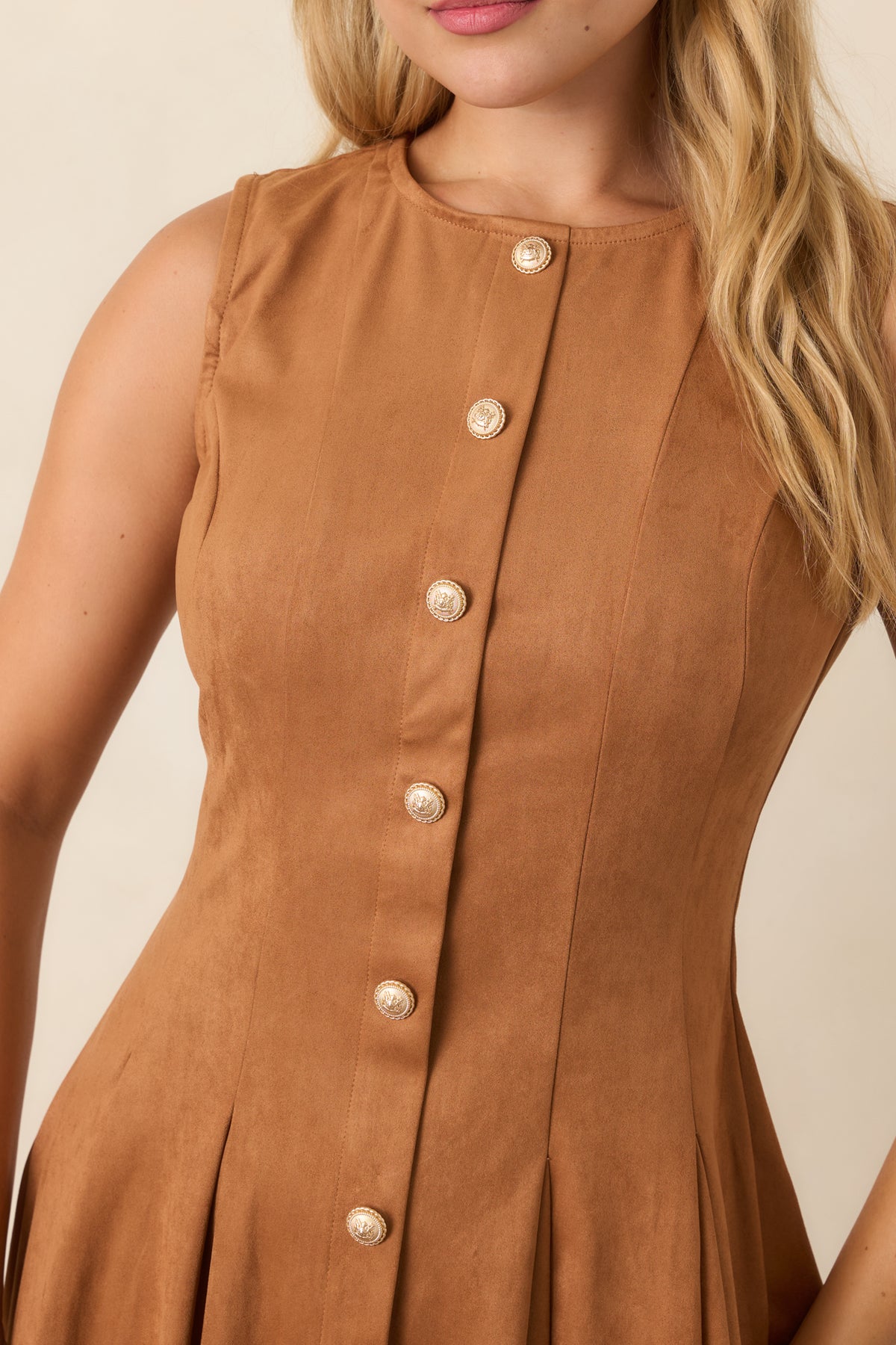 Close-up of the camel faux suede dress showing the ornate gold-tone buttons, tailored princess seams, and pleated skirt texture.