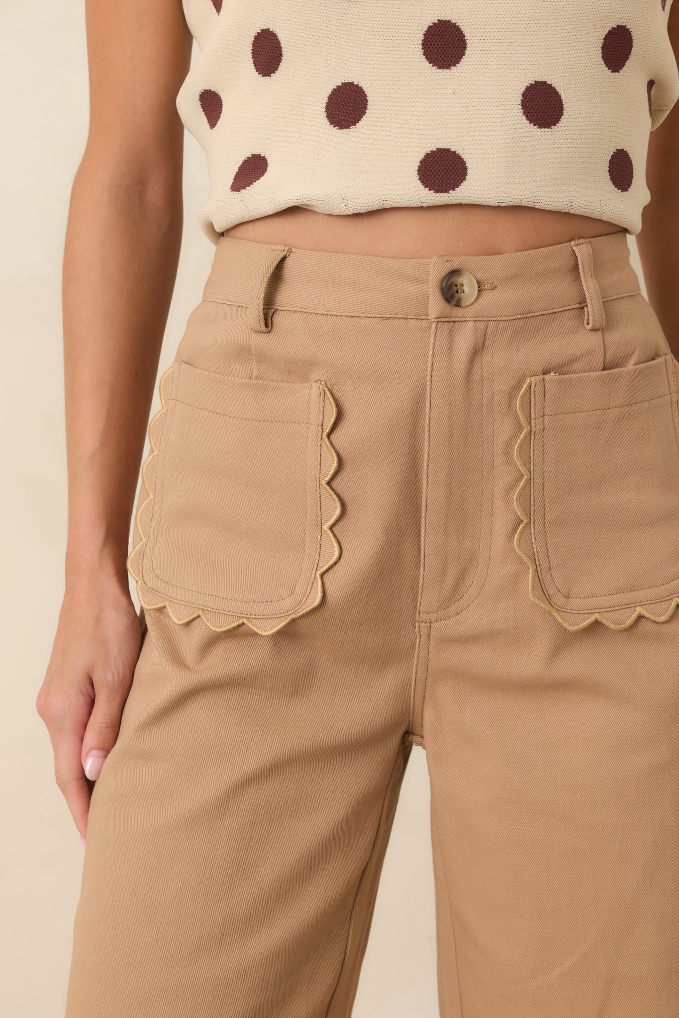 Close-up of the camel pants featuring the scalloped pocket edge, fabric texture, and polished front detailing.