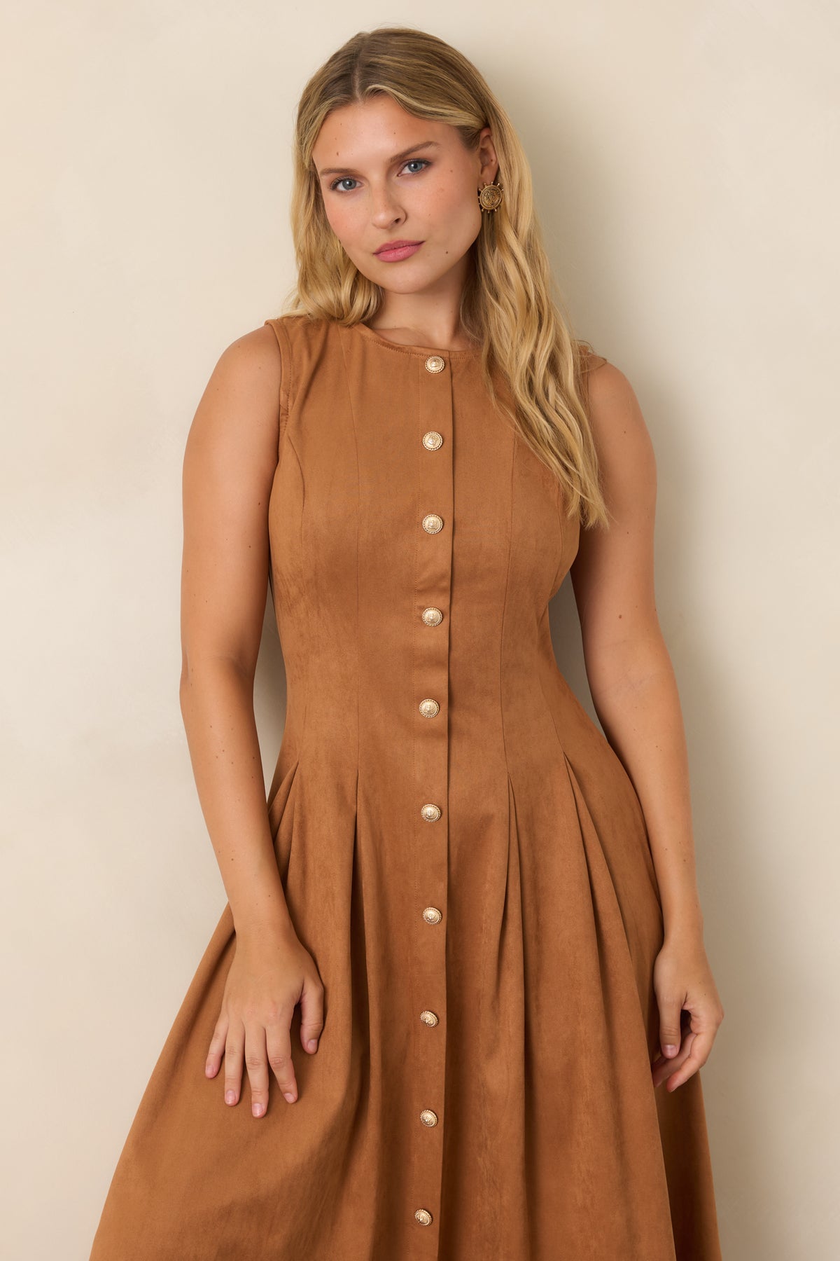 Sleeveless camel faux suede midi dress with a polished round neckline, fitted princess-seamed bodice, decorative gold-tone buttons, and flowing pleats.
