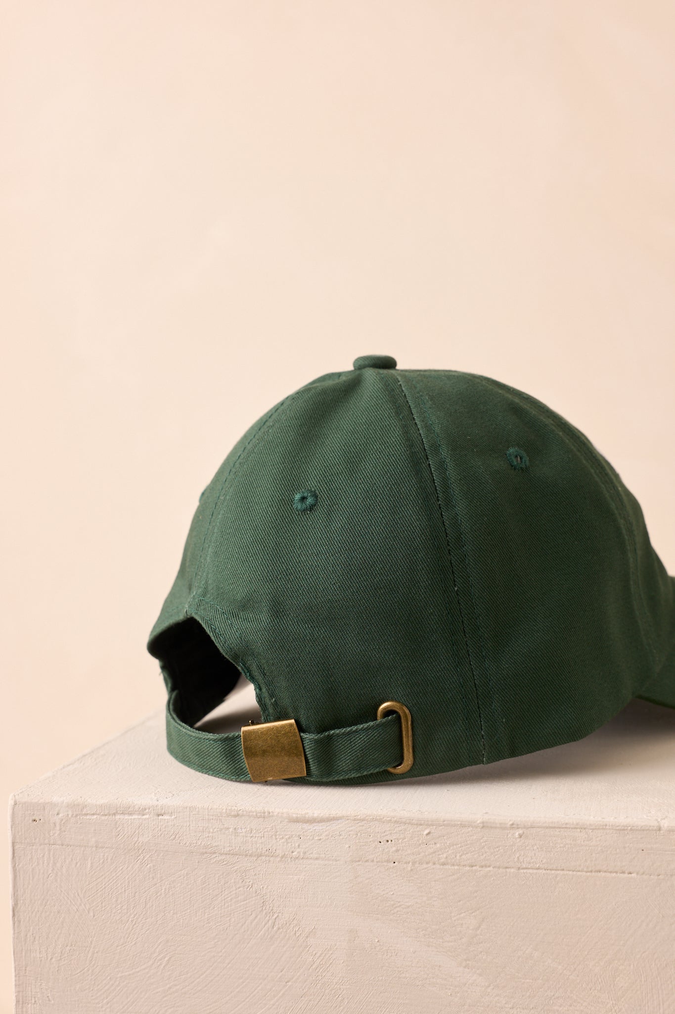 A back view of the cap showing the adjustable strap with a brass slide buckle closure.