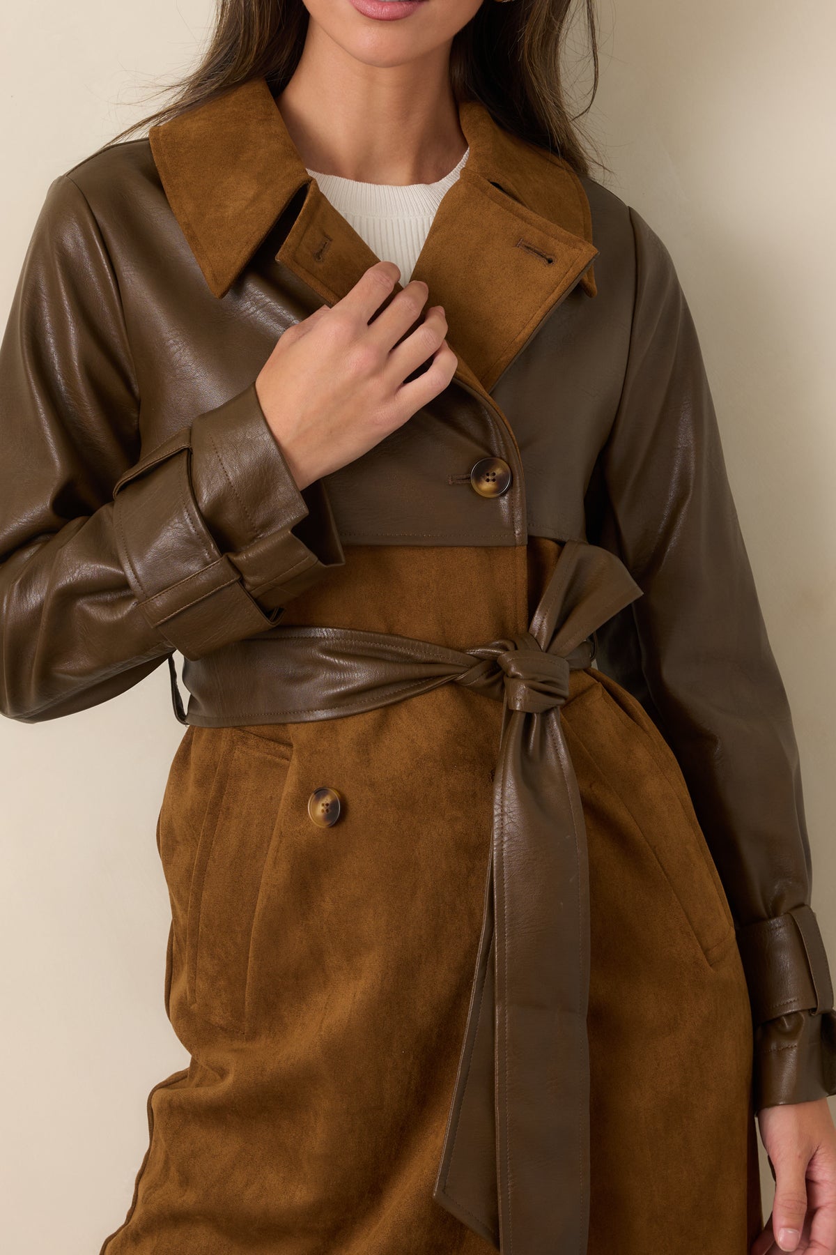 Close view of the caramel suede-look texture, wide lapel, double-breasted buttons, and contrasting brown faux leather sleeve.
