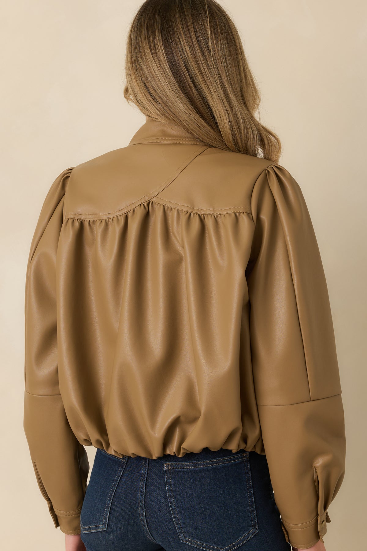 Rear view of the caramel vegan leather jacket featuring gathered back yoke detailing, long puff sleeves, and an elasticized hem.