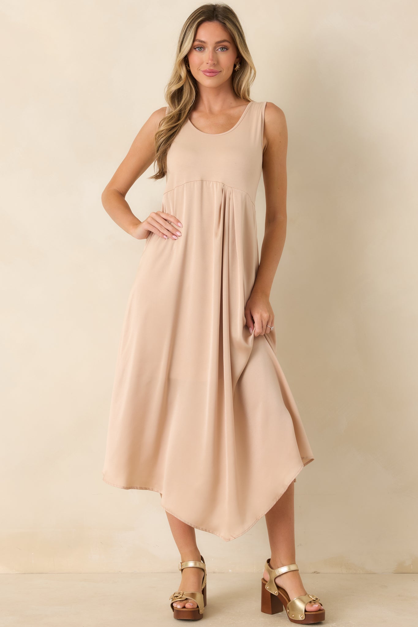 Full-length view of a champagne midi dress featuring a stretch-knit bodice, lustrous satin skirt, scoop neckline, and sleeveless silhouette.
