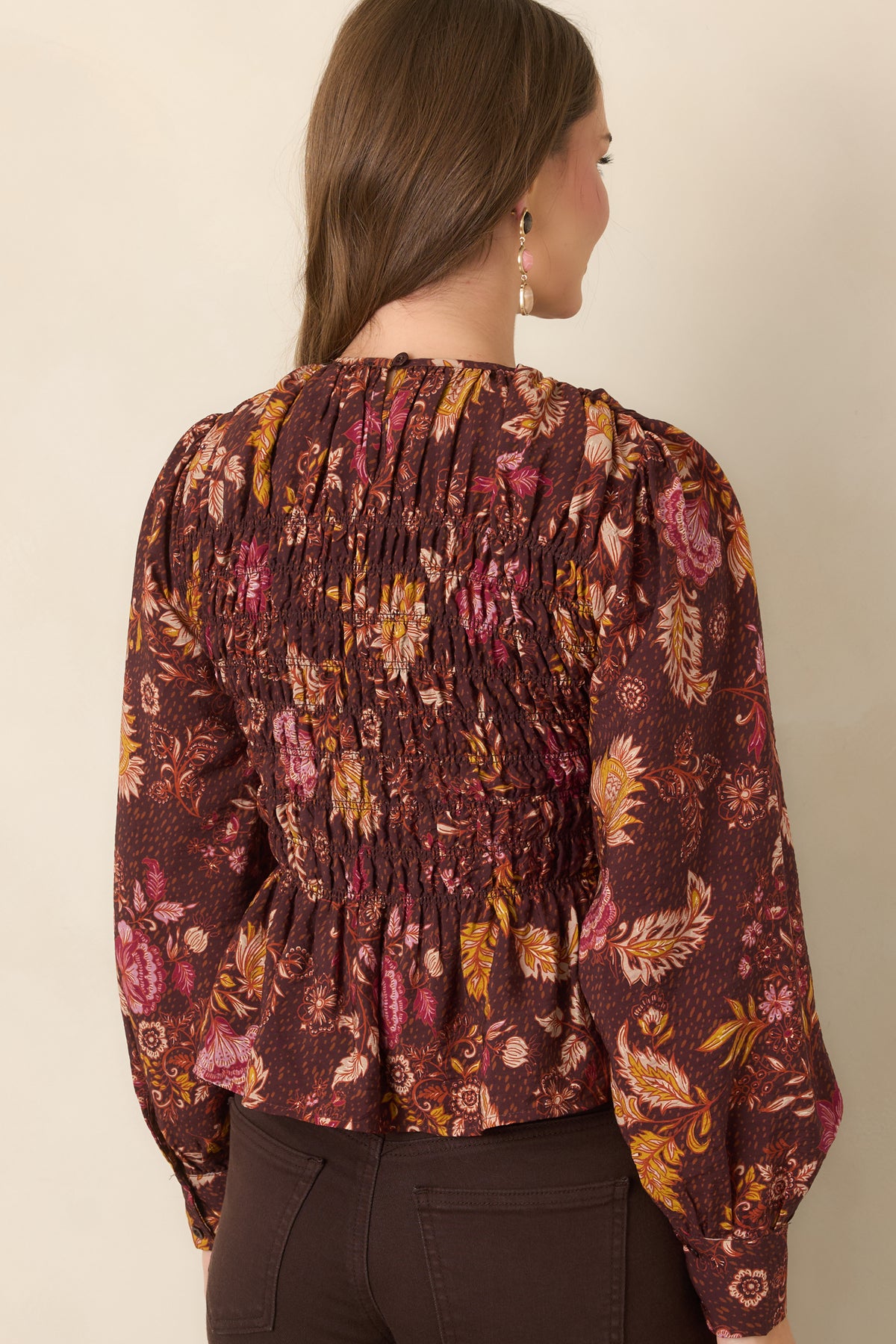 Rear of the chocolate brown floral top showing the smocked bodice, long puff sleeves, flared peplum hem, and back keyhole button closure.