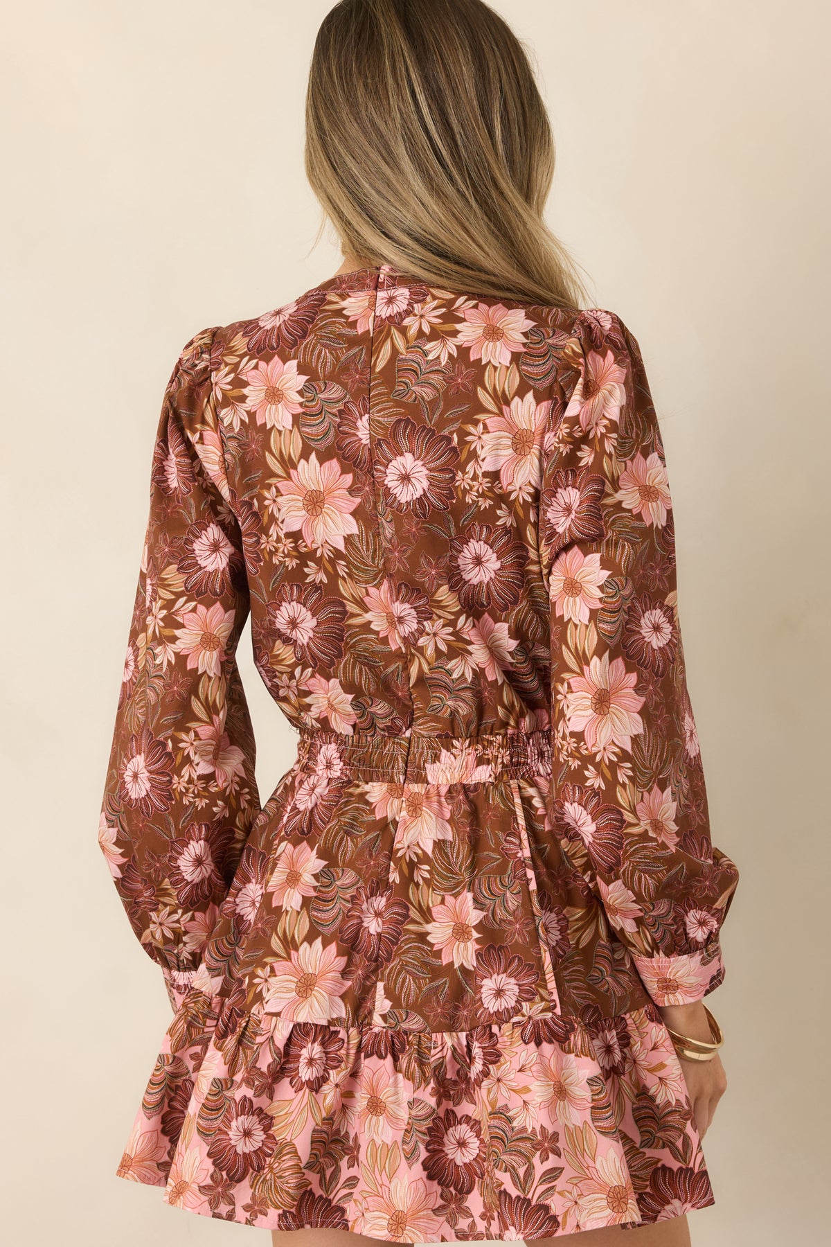 Rear view of the chocolate brown floral mini dress, showcasing its long sleeves, gathered waist, tiered skirt, and flowing silhouette.