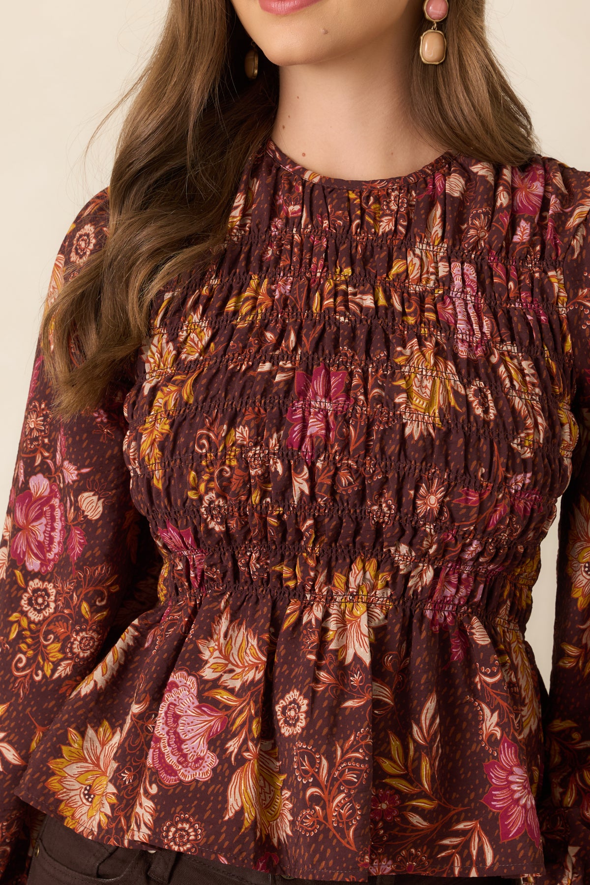 Close-up of the smocked bodice and warm floral print featuring pink, ivory, rust, and golden yellow blooms against a chocolate brown background.