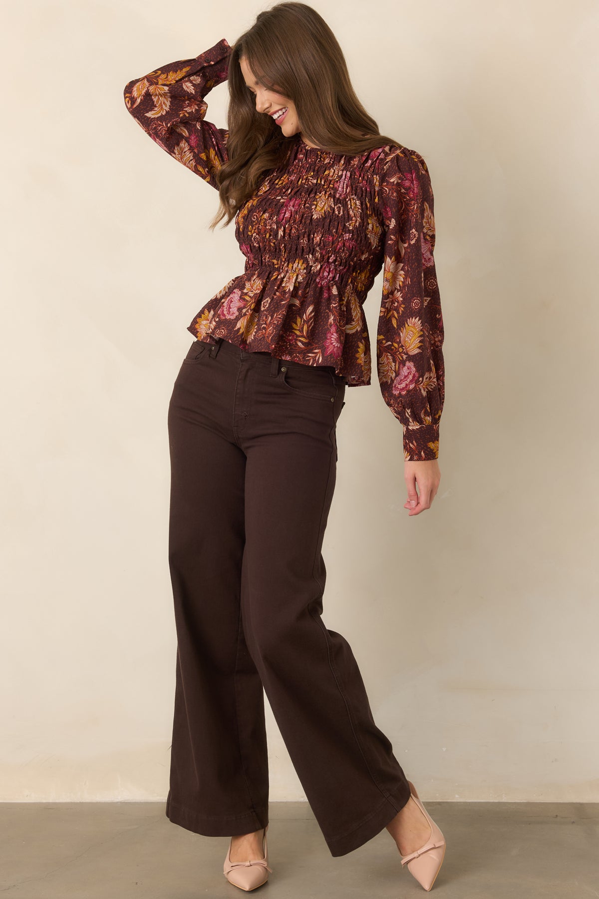 Chocolate brown floral top with a softly flared peplum silhouette, round neckline, smocked bodice, long puff sleeves, and tailored button cuffs.