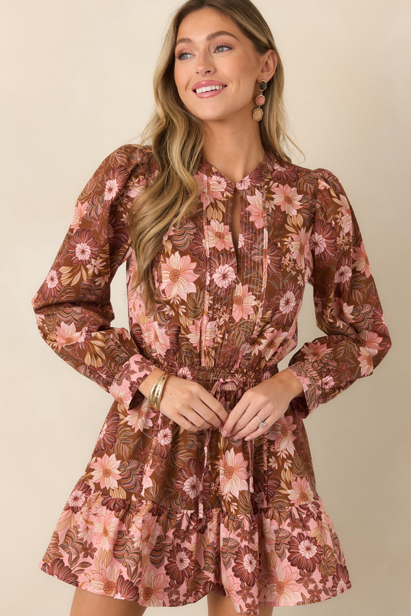 Chocolate brown floral dress highlighting the split neckline, gathered drawstring waist, and long sleeves finished with button cuffs.