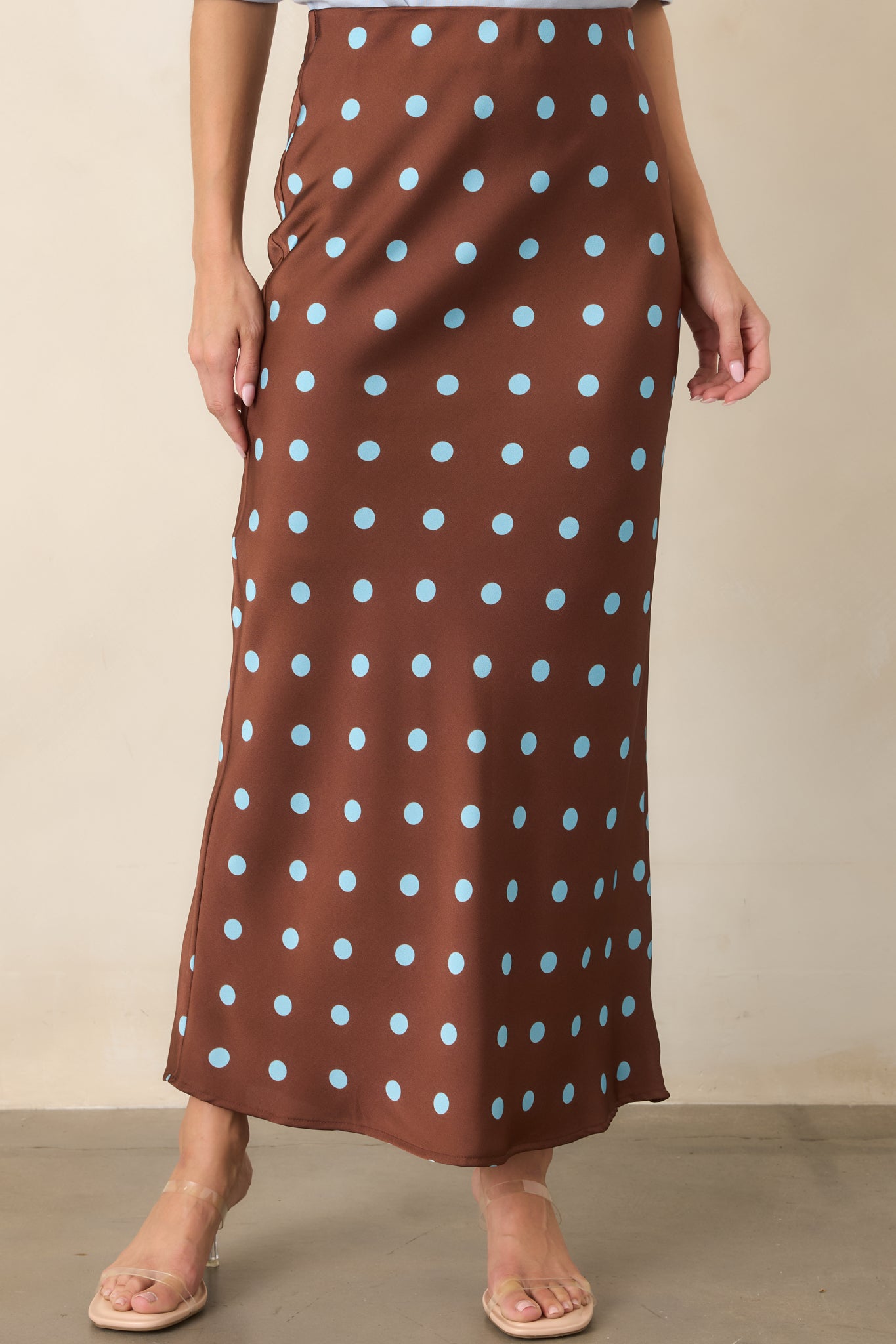 Chocolate brown satin skirt highlighting its elastic waistband, smooth bias-cut construction, and light blue polka dot pattern.