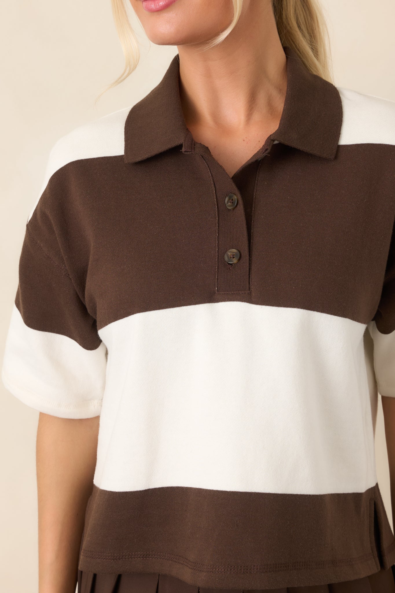 Close-up of the collared neckline and short button placket, framed by contrasting dark chocolate and ivory horizontal panels.