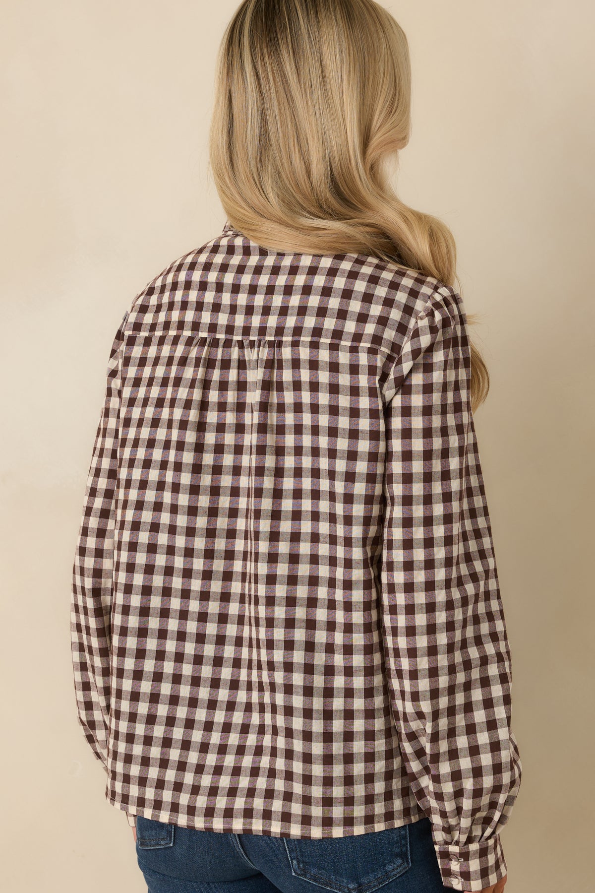 Back of chocolate and ivory gingham blouse featuring a structured back yoke, center pleat, and long sleeves.