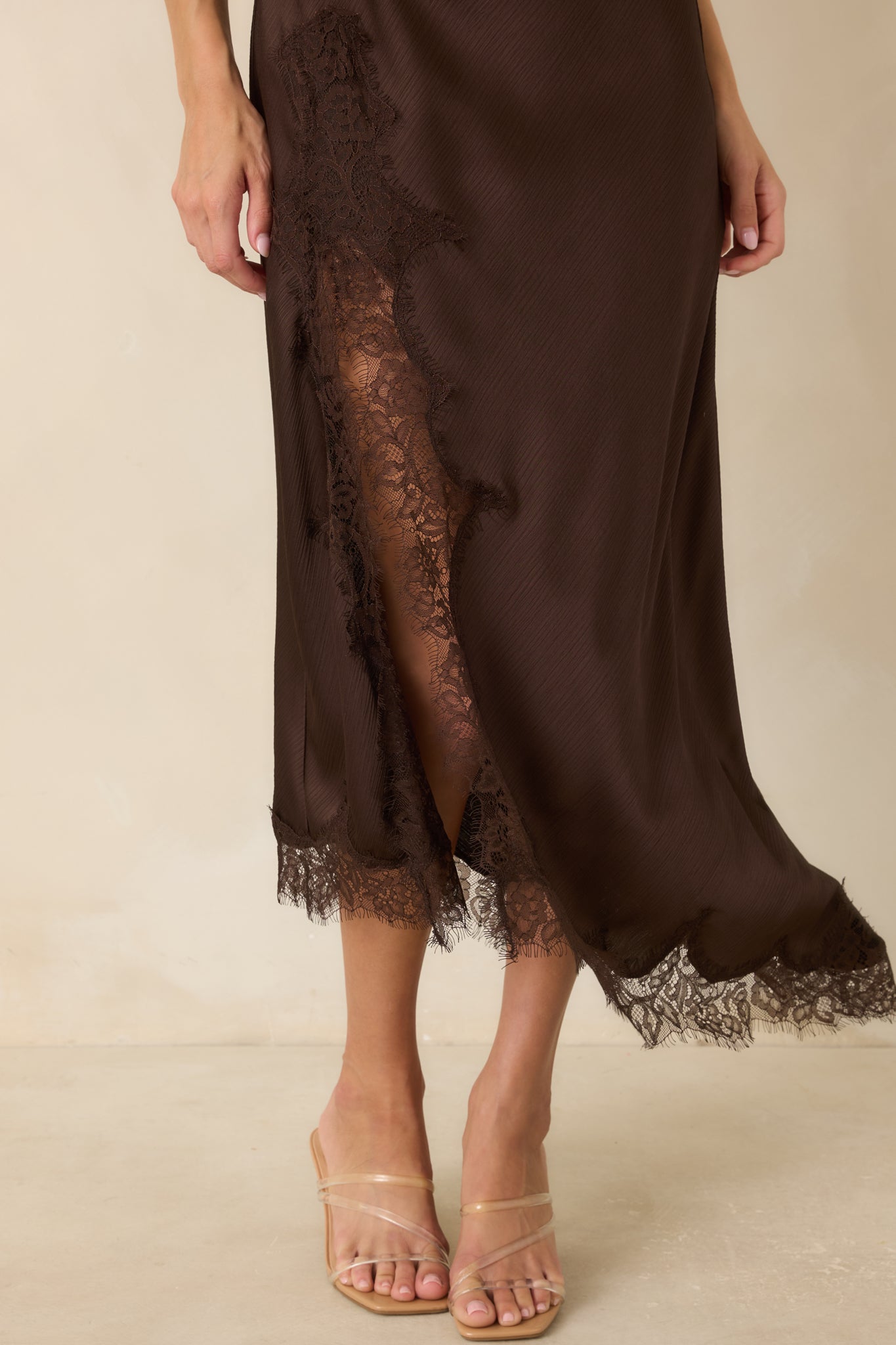 Close-up of the asymmetrical bottom hem showcasing delicate eyelash lace trim and the flowing chocolate satin fabric.