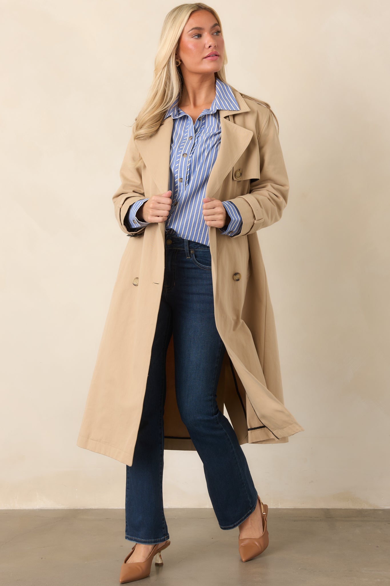 Classic tan trench showcasing a structured storm flap, adjustable buckled cuffs, button-front closure, and versatile belted waist.