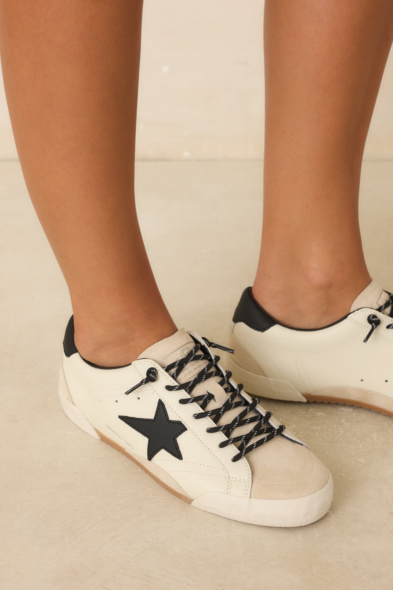 Classic white sneakers showcasing black star and heel details, a low-profile silhouette, mixed materials, and a worn-in finish.