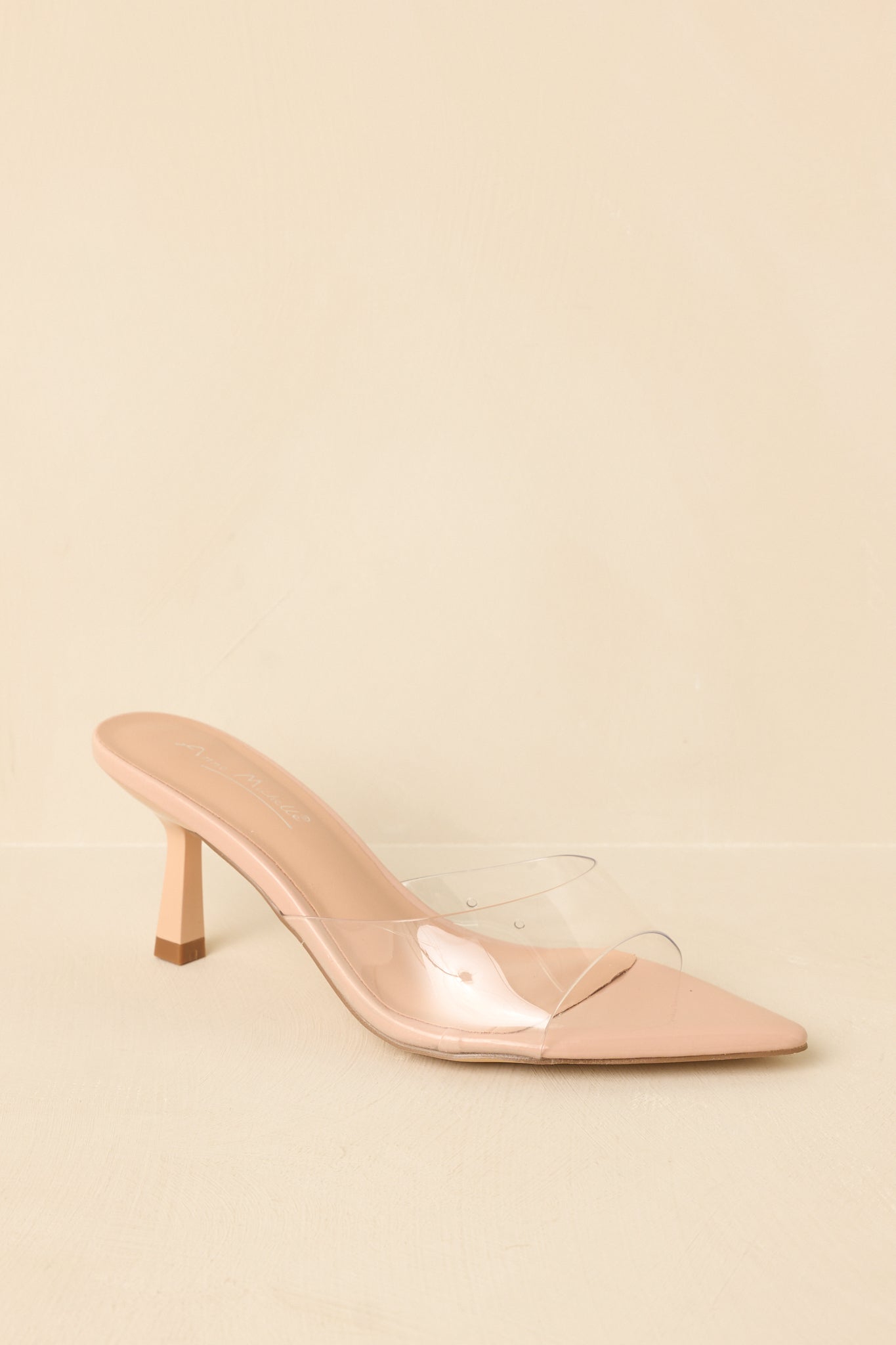 Side view of clear nude kitten heel mules displayed on a beige background, showing the pointed toe and subtle lift.