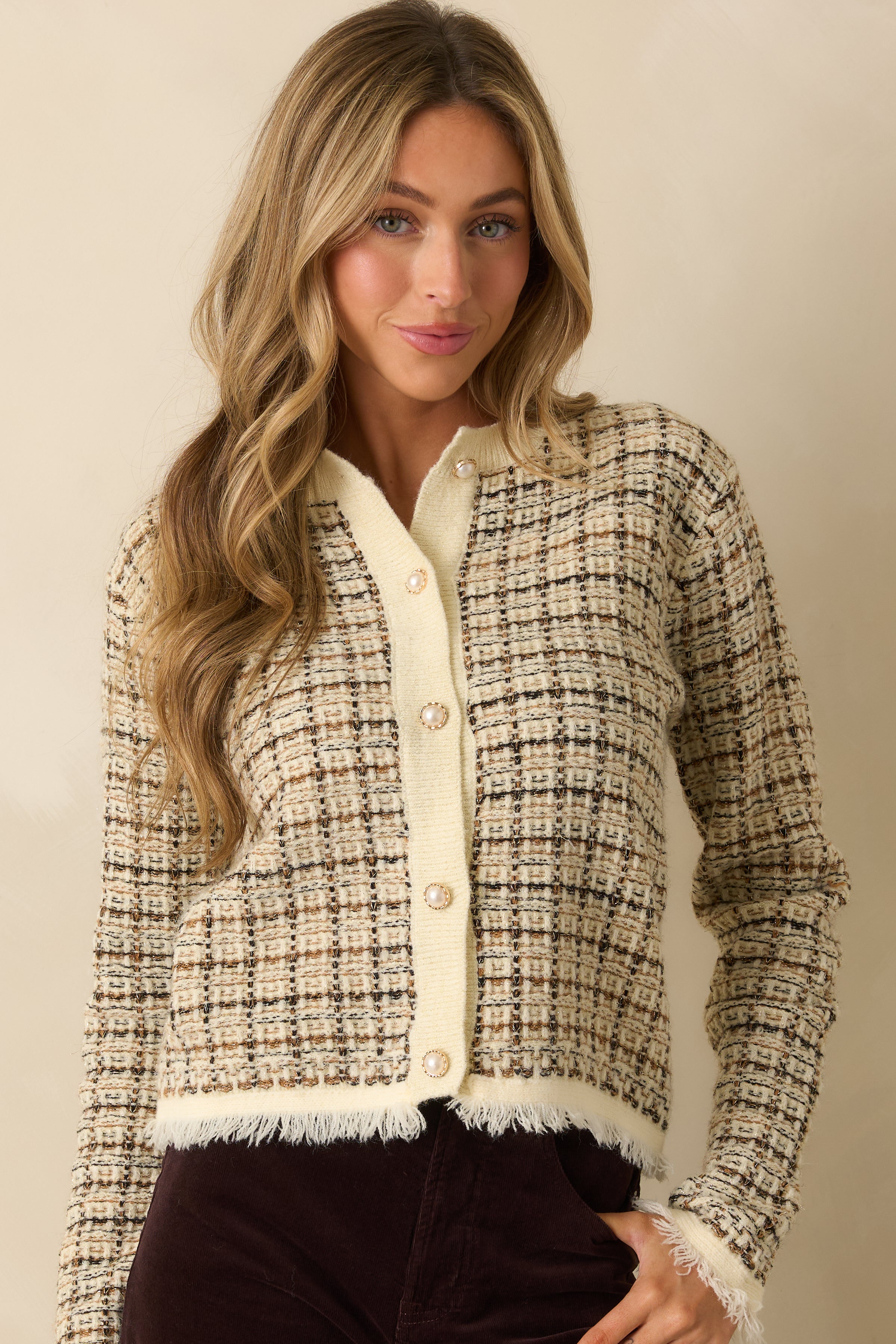 Close crop of cardigan’s pearl-accented button closure and ribbed trim, highlighting the woven plaid pattern in black, caramel, and gold.