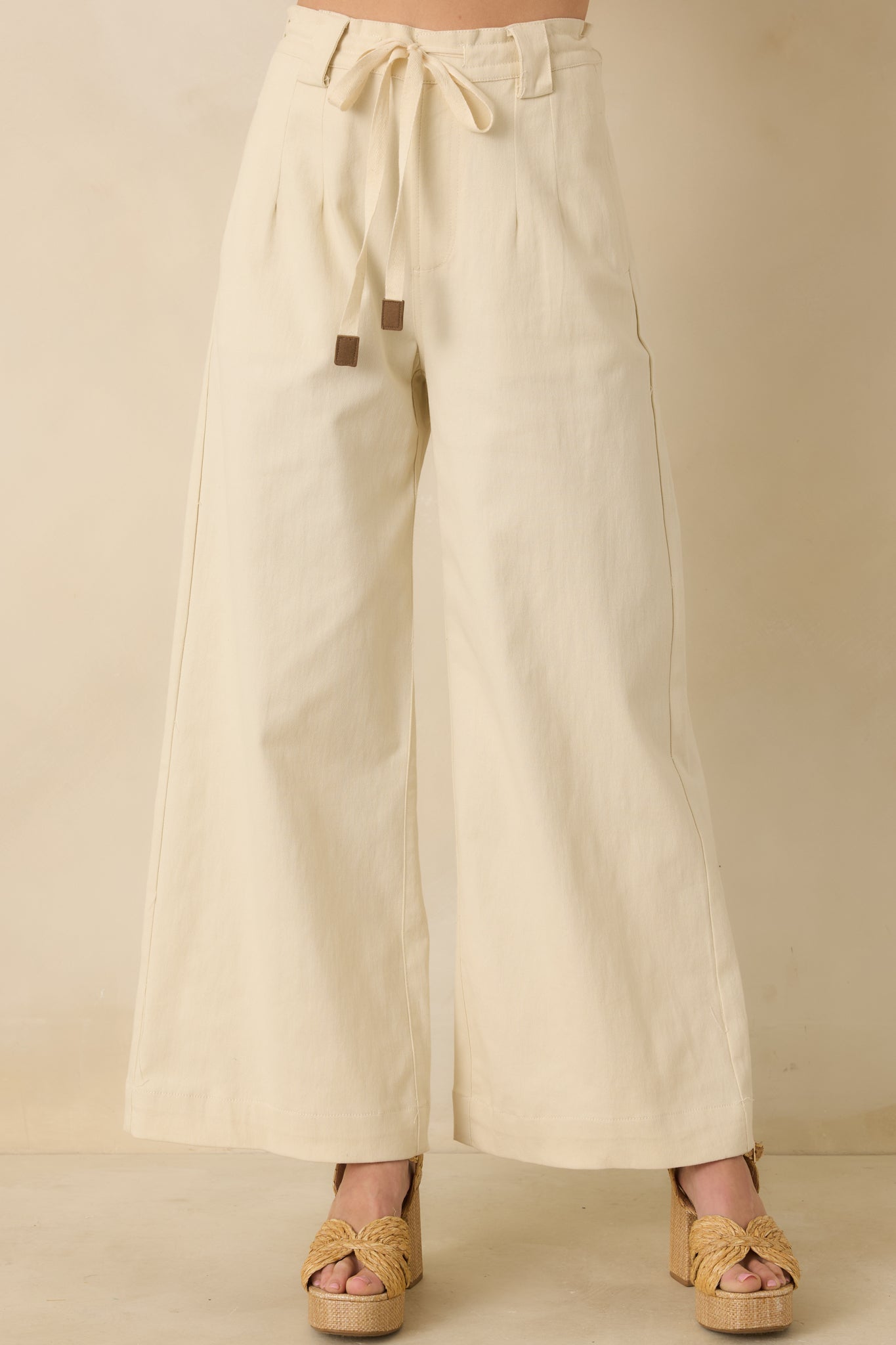 Close crop highlighting the fabric texture and relaxed flow of the beige wide-leg pants.