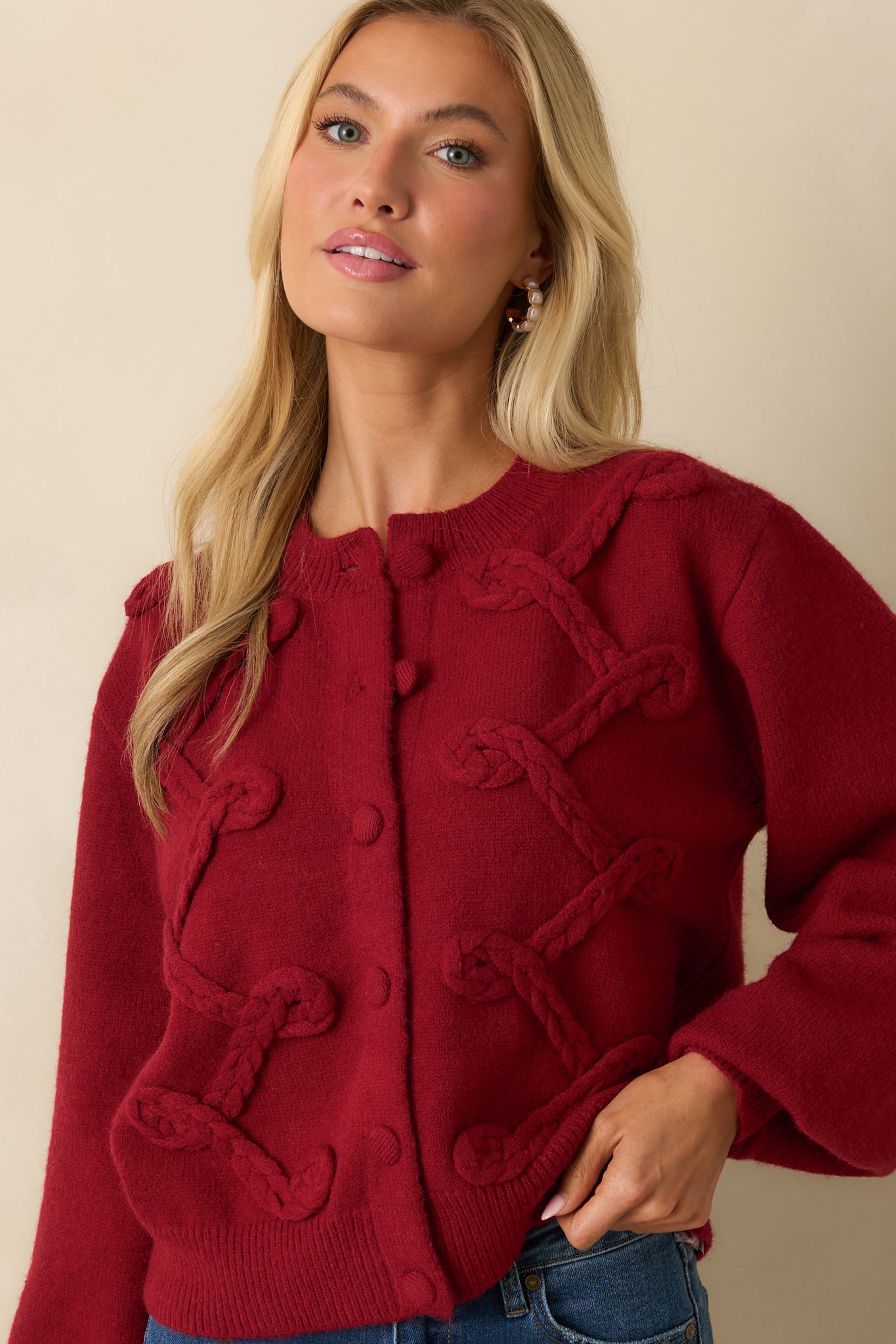 Close crop focusing on the textured braided detailing and button closures on the red knit cardigan.