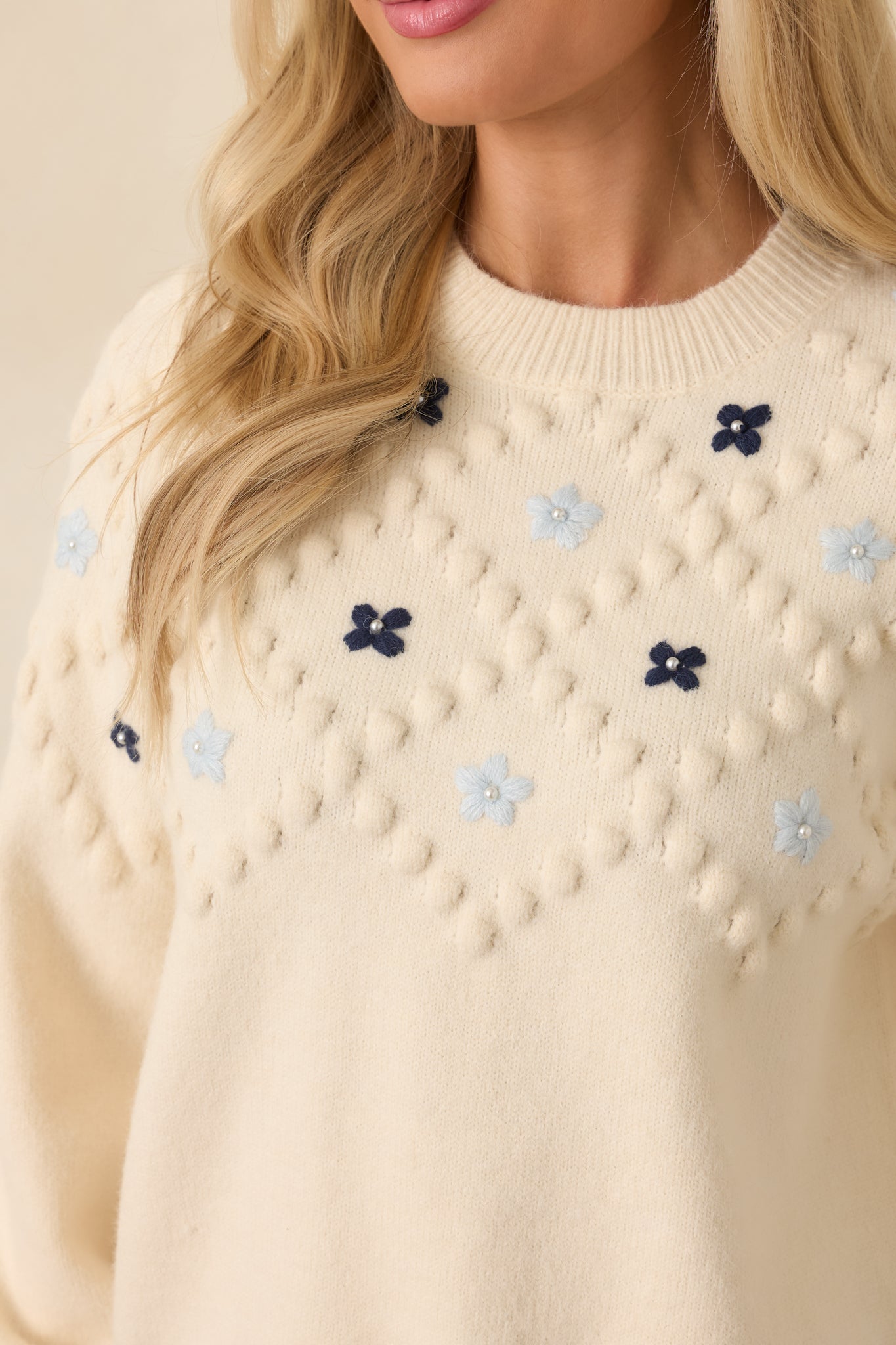 Close detail of the raised bobble knit texture with intricate multicolor floral embroidery stitching.