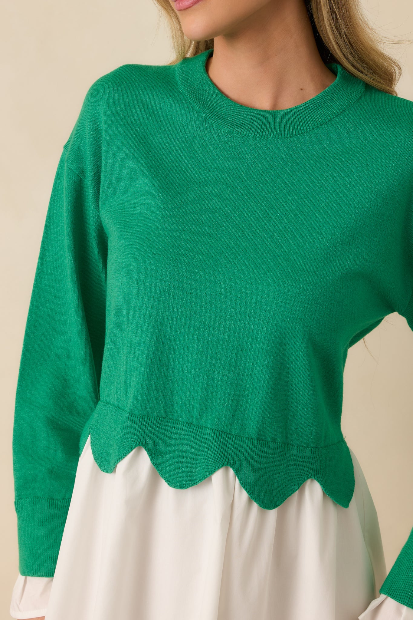 Close-up detail of the green and white mini dress showing the scalloped hem at the waist and textured knit fabric.