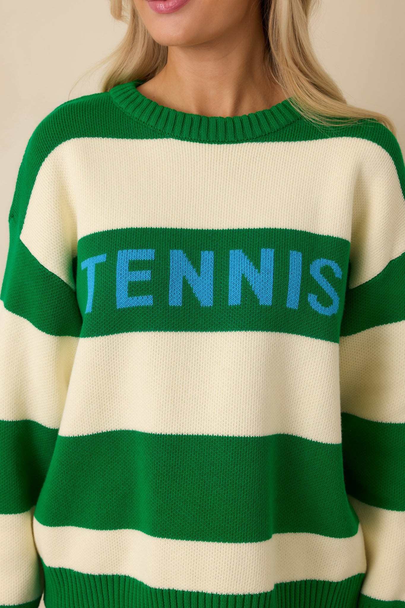 Close-up of the knit texture and “TENNIS” lettering with ribbed hem detailing on the sweater.