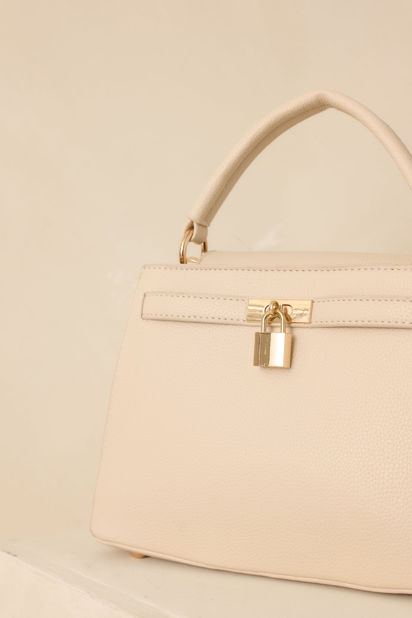 Close-up of the magnetic button closures and decorative lock detail on the nude faux leather handbag.