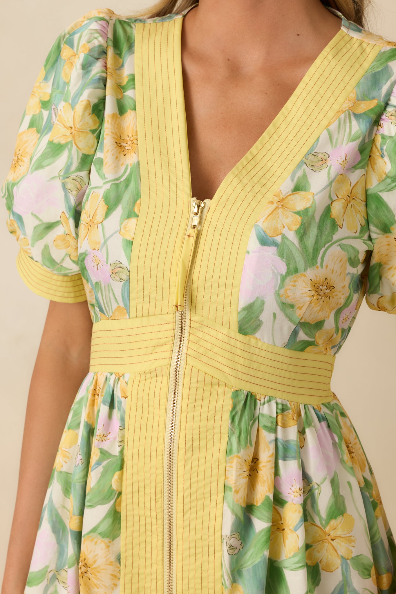 Close-up of the yellow floral print, zip-front V-neckline, and cuffed short puff sleeves, showing fabric texture and design details.
