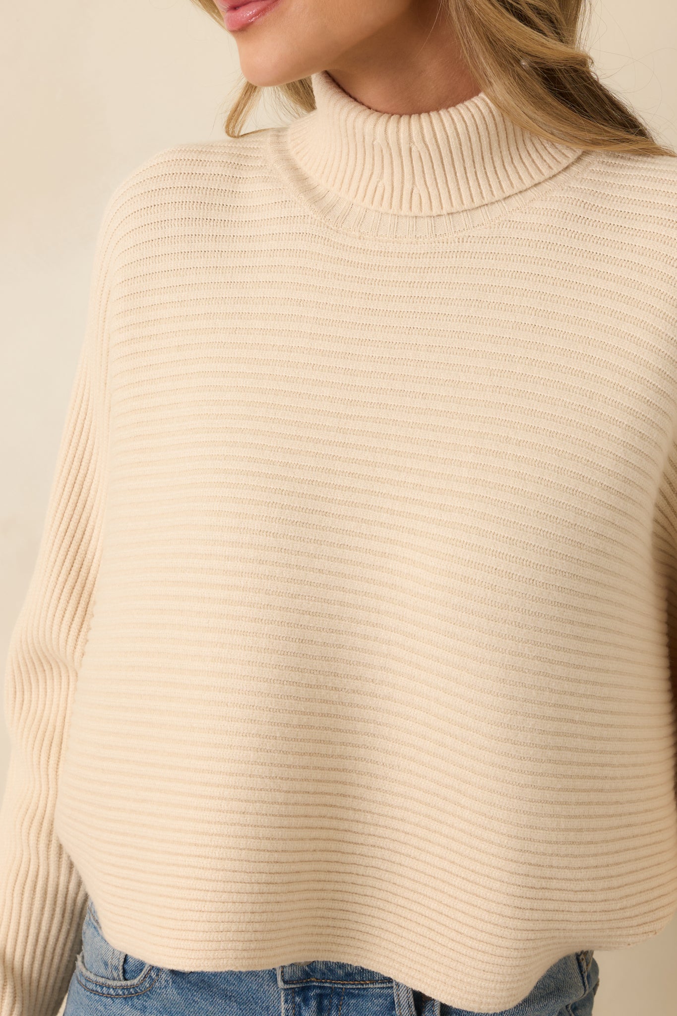 Close-up of turtleneck and ribbed knit fabric highlighting soft texture of beige sweater.