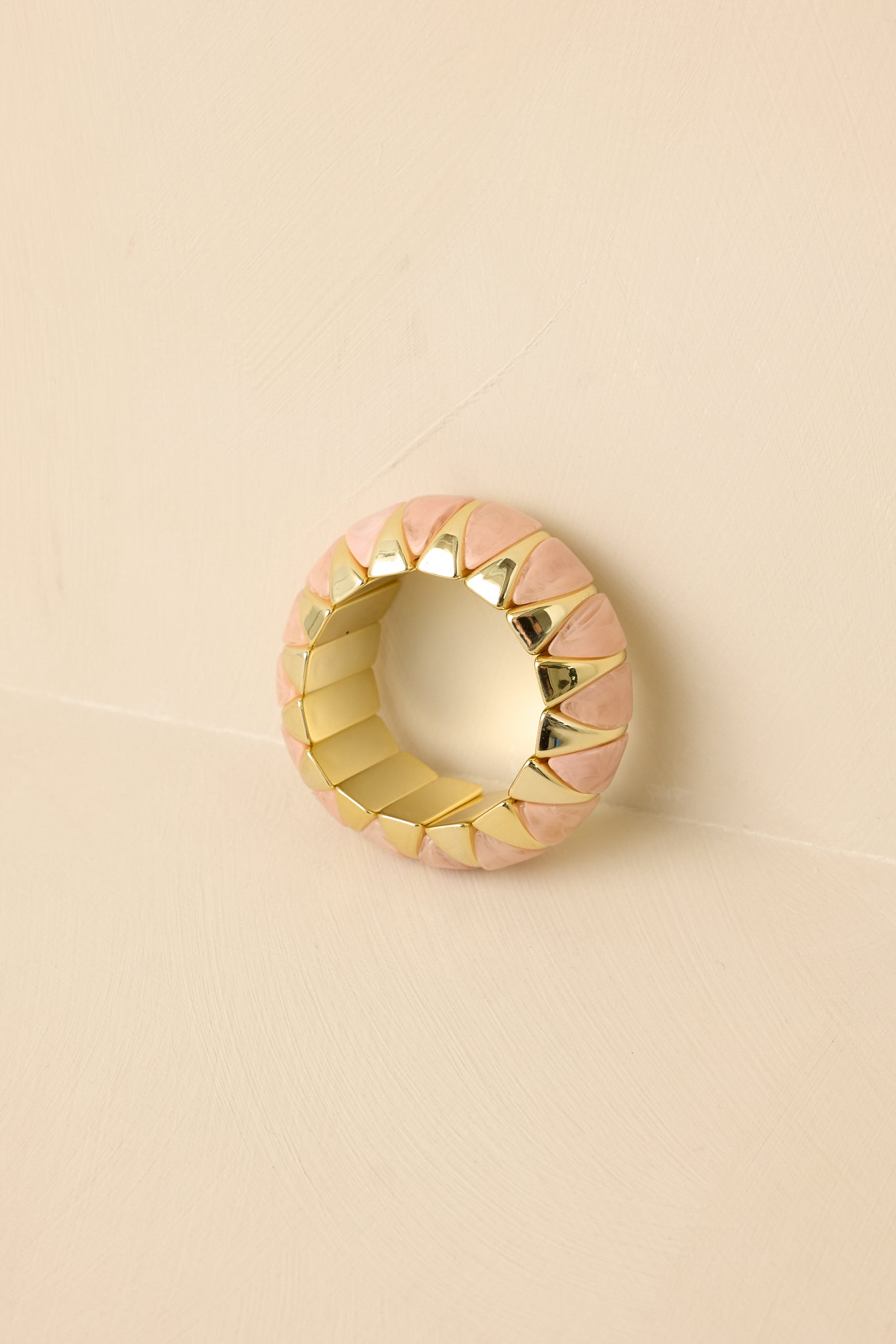 Close-up crop showing bracelet’s smooth rounded gold settings cradling pink beads.