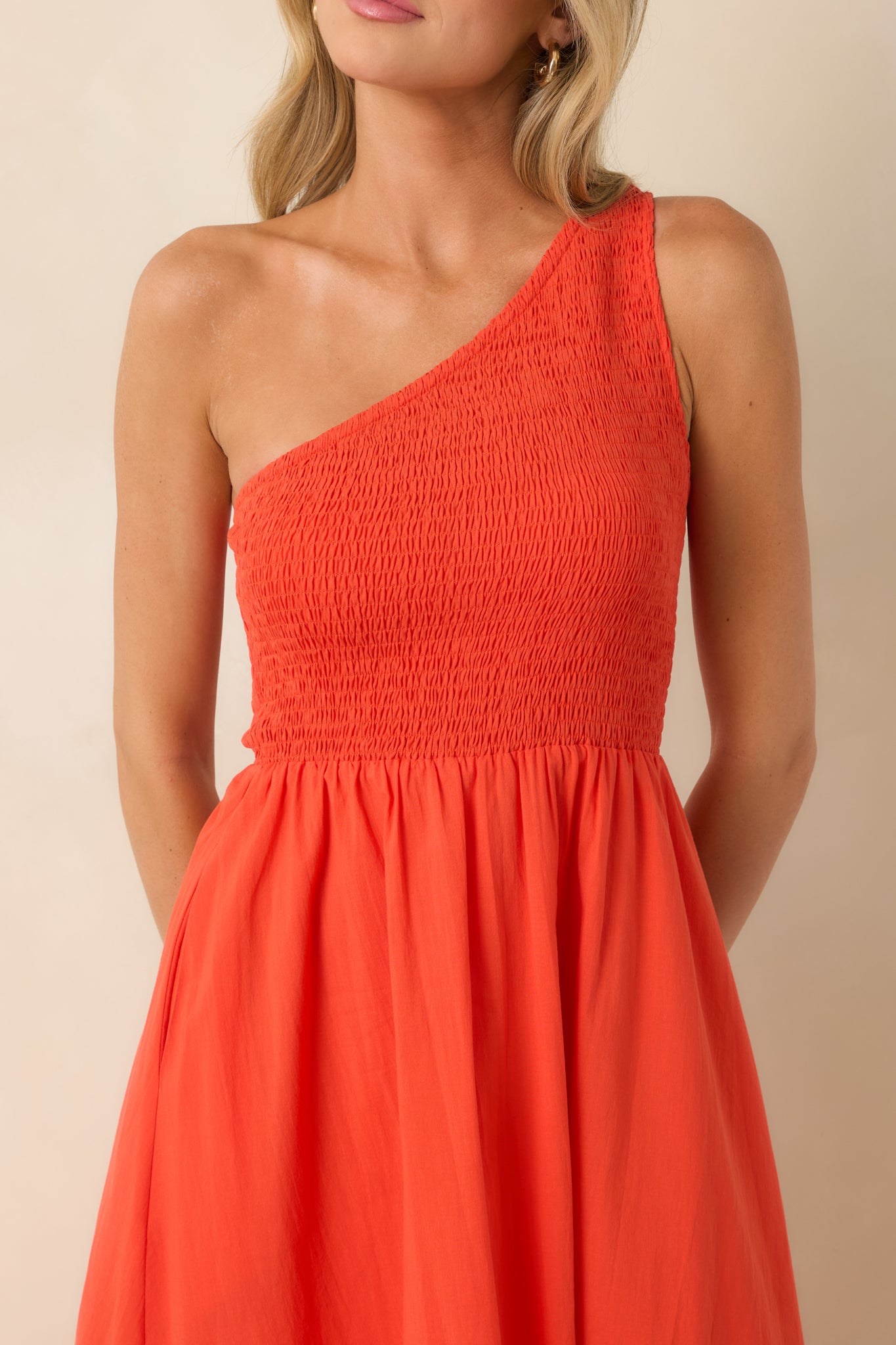 Close-up of the coral-orange maxi dress highlighting the fully smocked bodice, one-shoulder neckline, breathable cotton fabric, and textured finish.