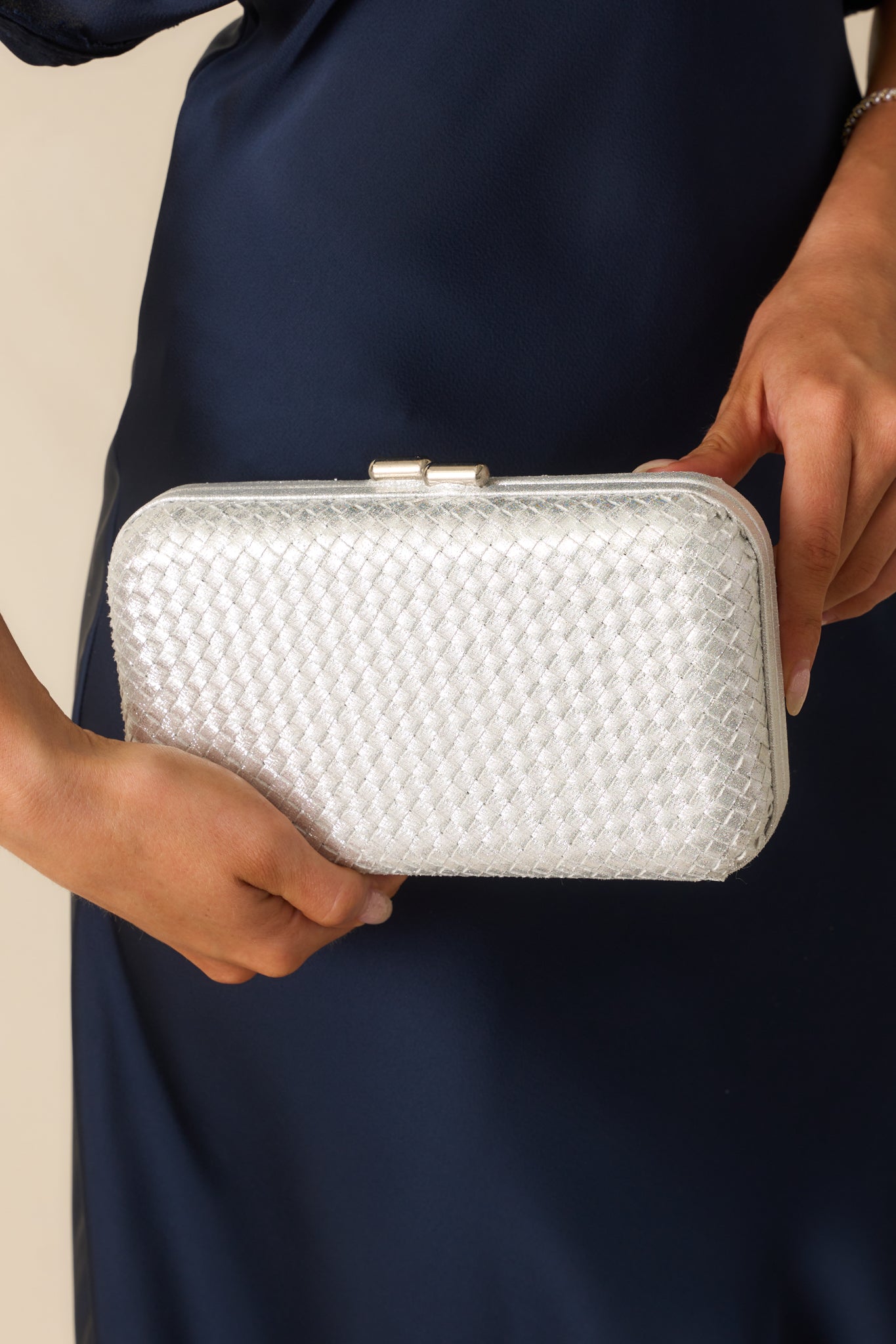 A close-up detail of the clutch highlighting the woven surface, clasp closure, and polished silver finish.