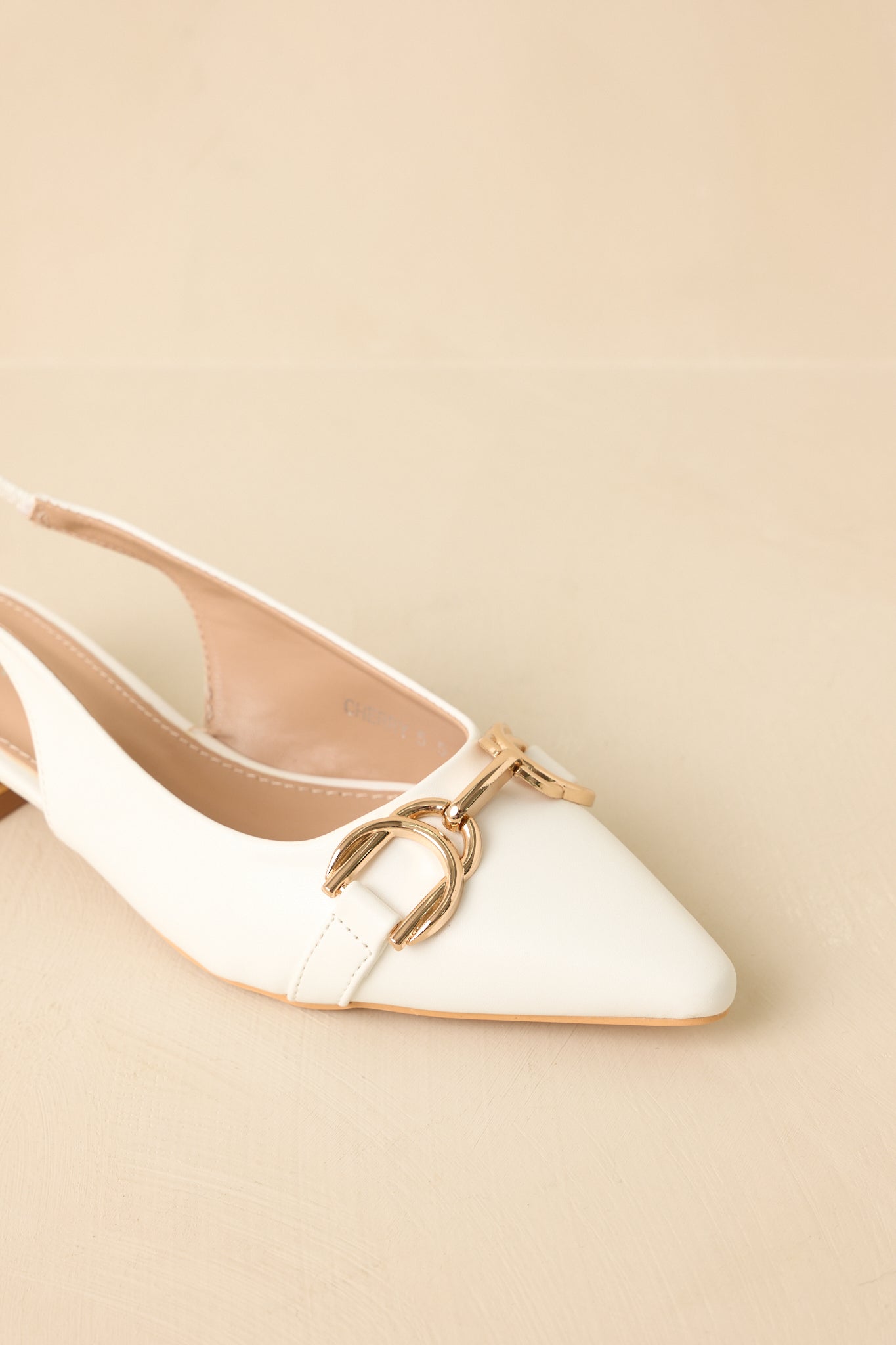 Close-up detail of the white slingback flats showing the gold-tone hardware accent and smooth faux leather finish.