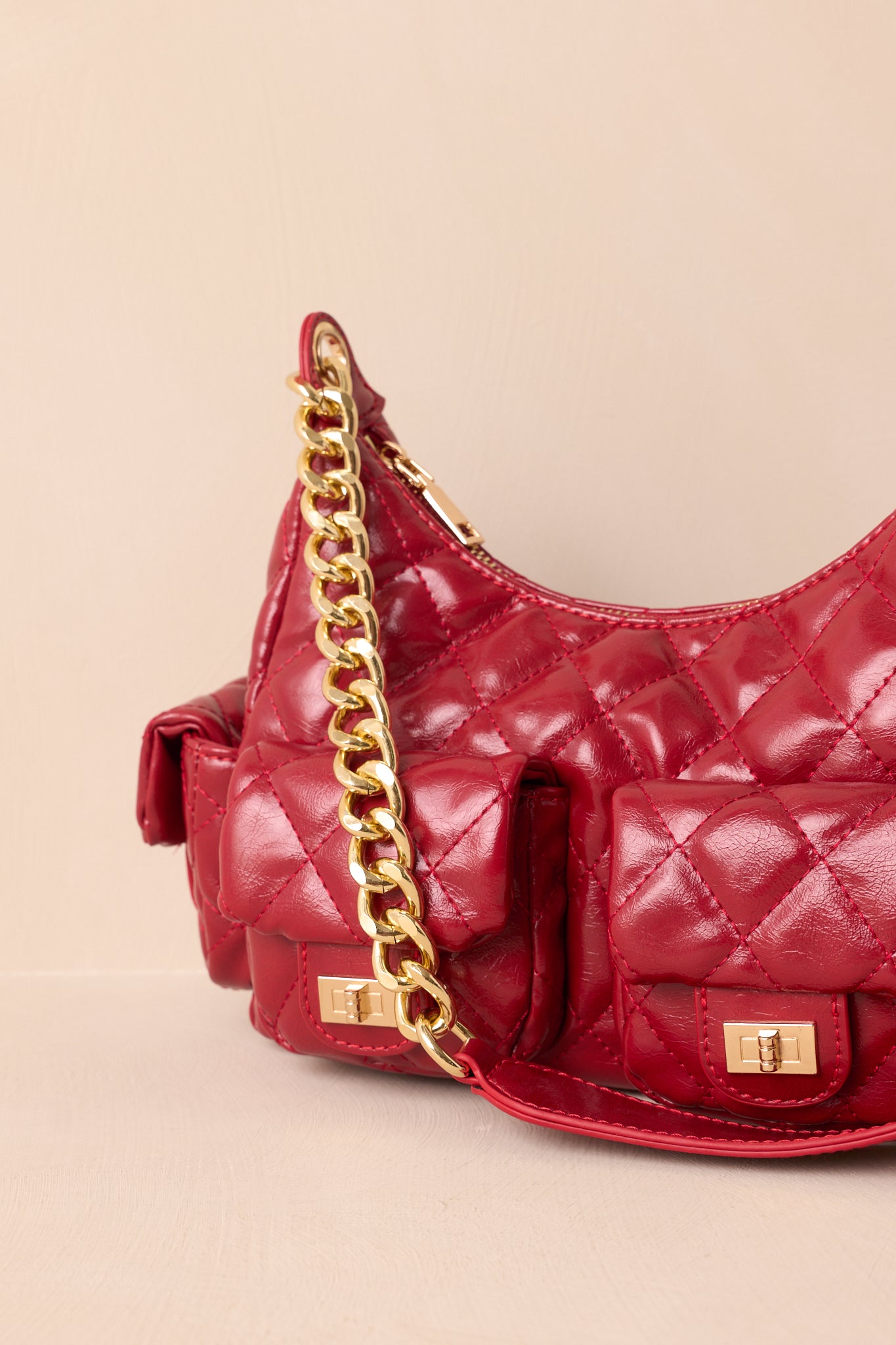 A close-up detail of the red handbag highlighting the gold turn-lock hardware, quilted stitching, and smooth finish.