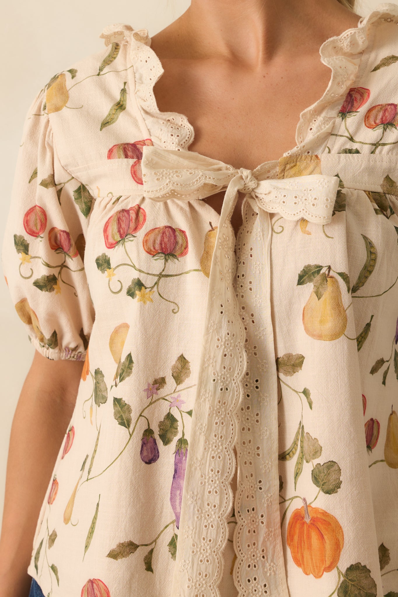 Close-up detail of ivory top’s scalloped lace ruffle, multicolored vegetable print, and soft fabric texture.