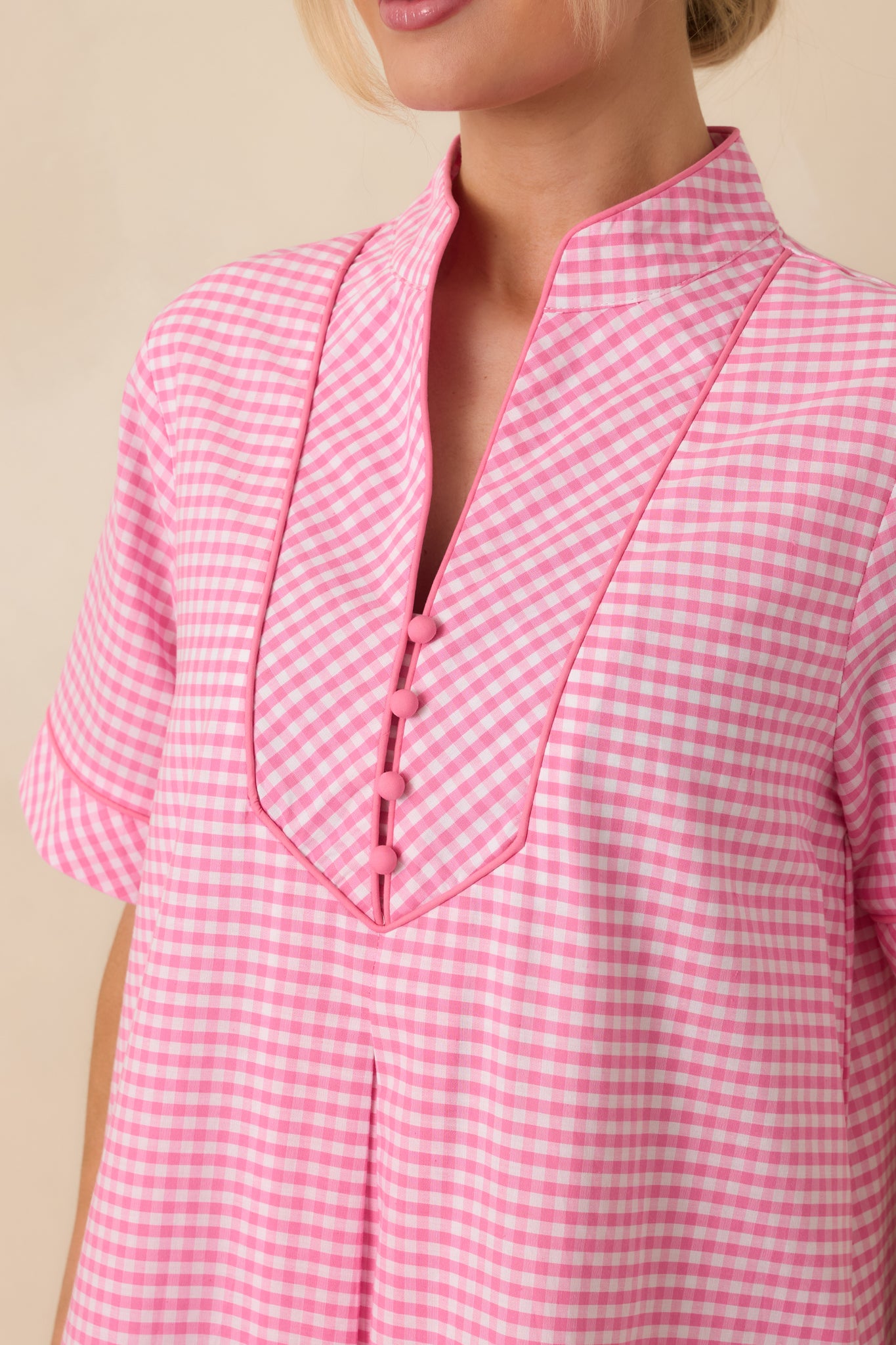 Close-up detail of the pink gingham maxi dress showing the V-neckline with contrast trim and fabric texture.