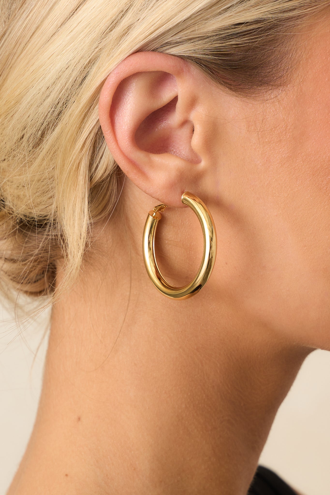 Extreme close-up of a single gold hoop earring, focusing on the hinged clasp and high-shine gold texture.