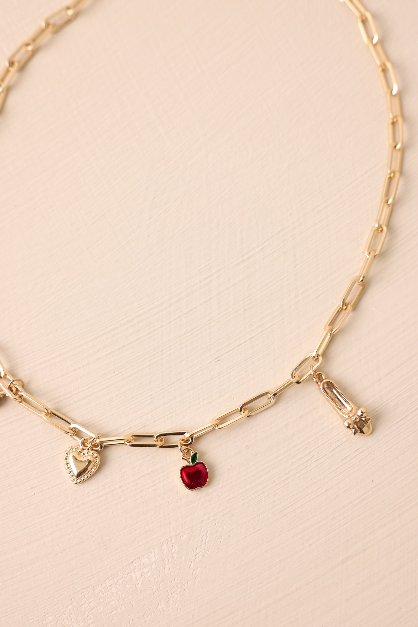 Detailed close-up capturing the textures of the gold charms, red apple enamel, and lobster claw clasp.