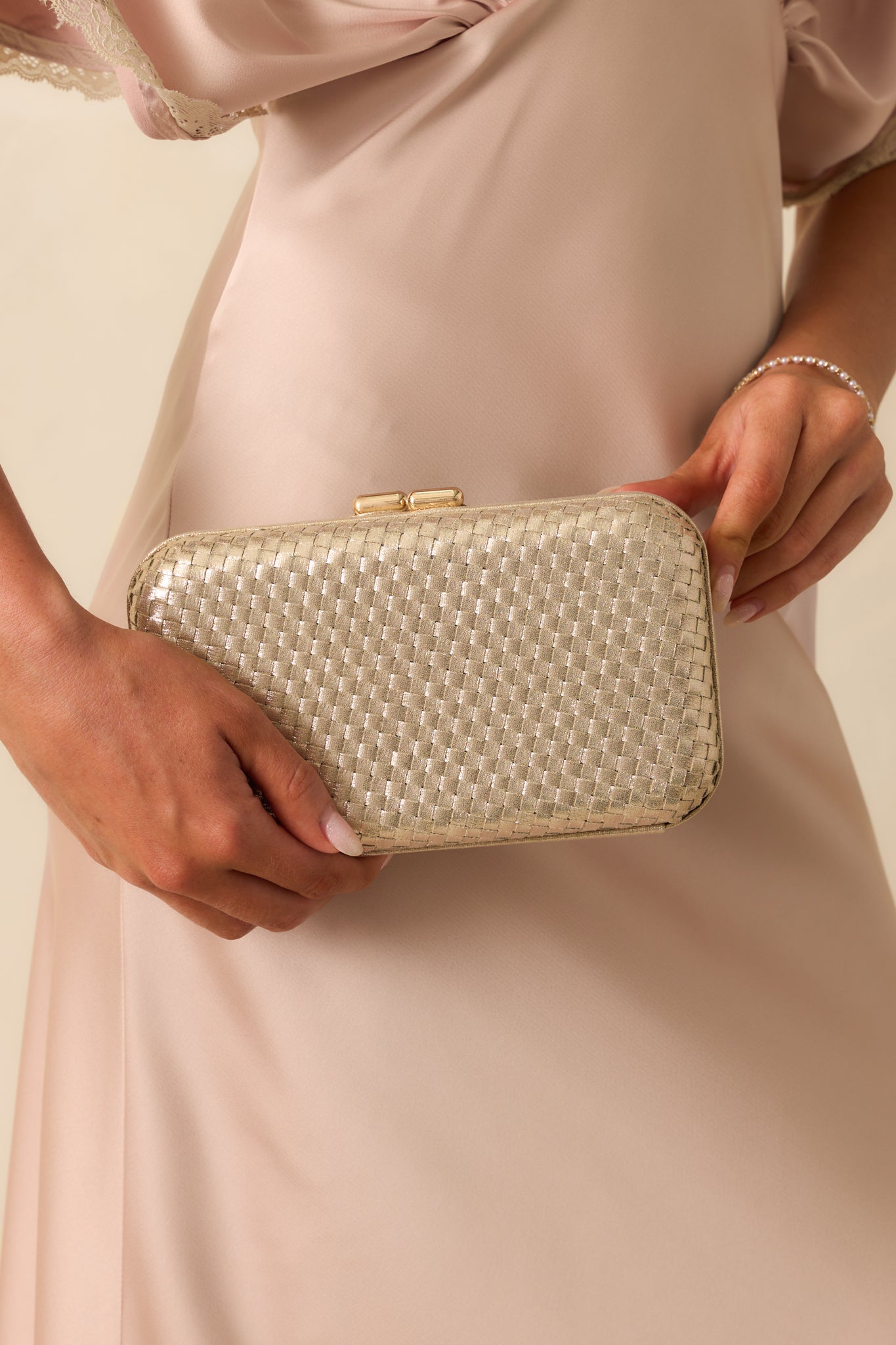 Close-up detail photo of the gold clutch emphasizing the hinged frame, woven texture, and metallic finish.