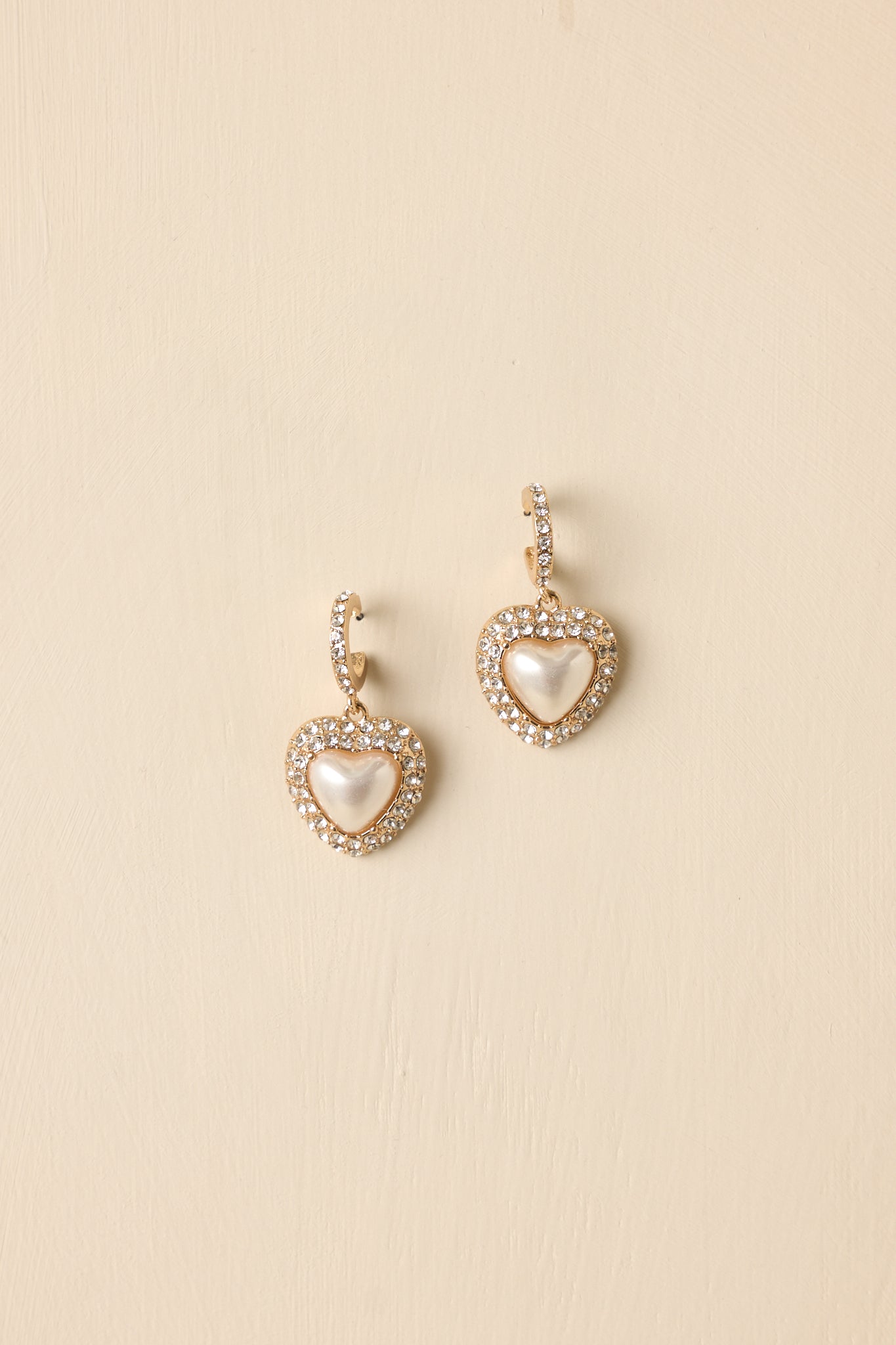 Detailed close-up of gold drop earrings focusing on the heart-shaped ivory pearl, surrounding rhinestones, and curved hook post.