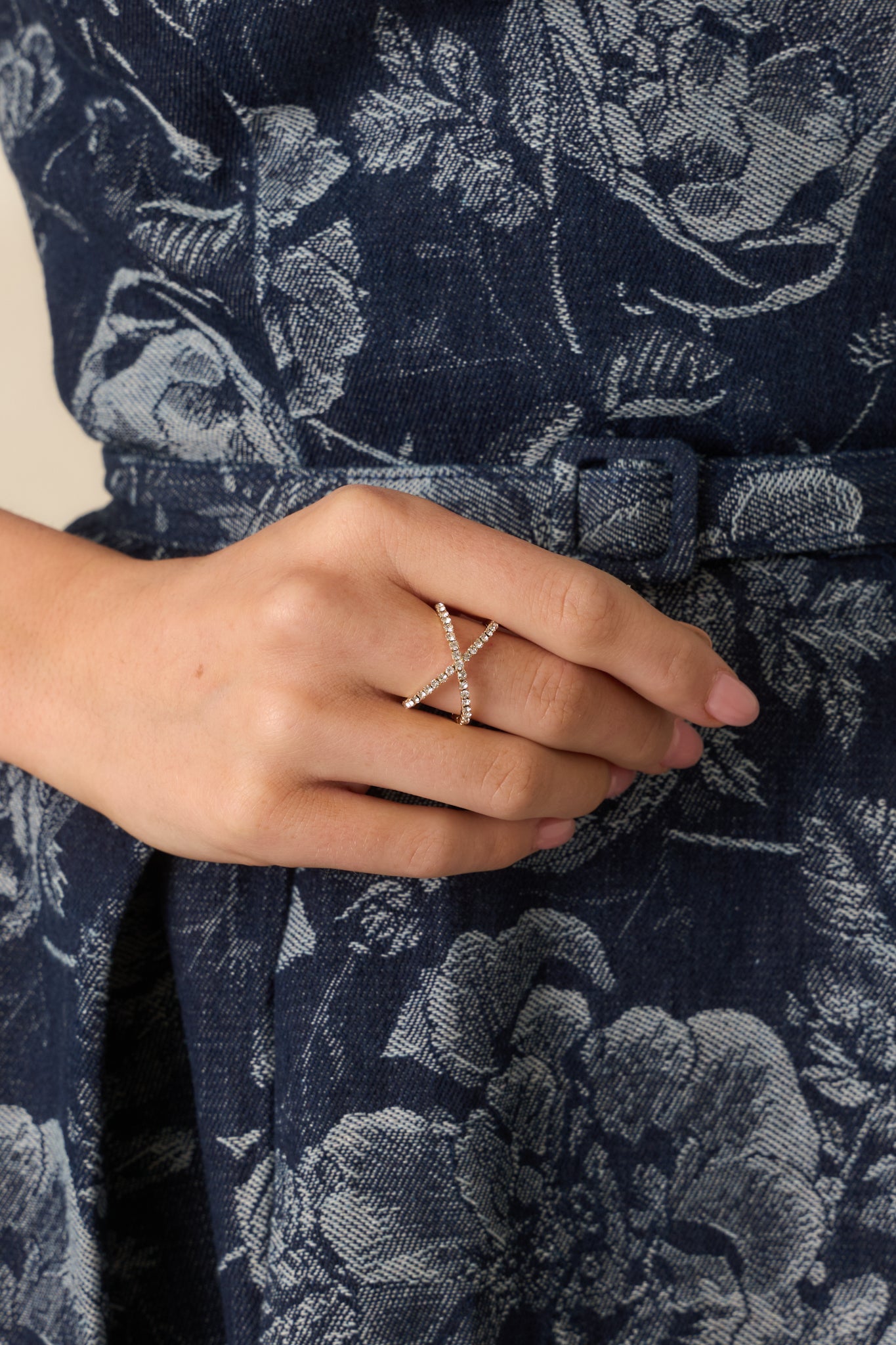 A close-up detail of the gold ring showing a polished metal finish, intersecting rows of clear rhinestones, and open band structure.