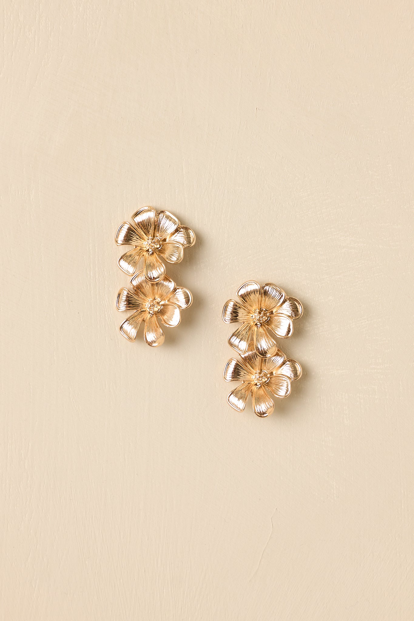 Detailed close-up of the gold-tone drop earrings focusing on the textured petals and layered double-flower design.