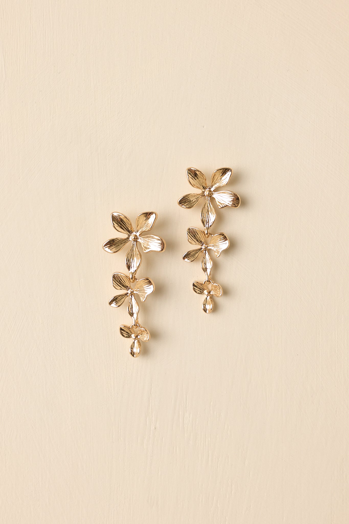 Detailed close-up of the gold-tone drop earrings focusing on the tiered floral structure and textured petal detailing.