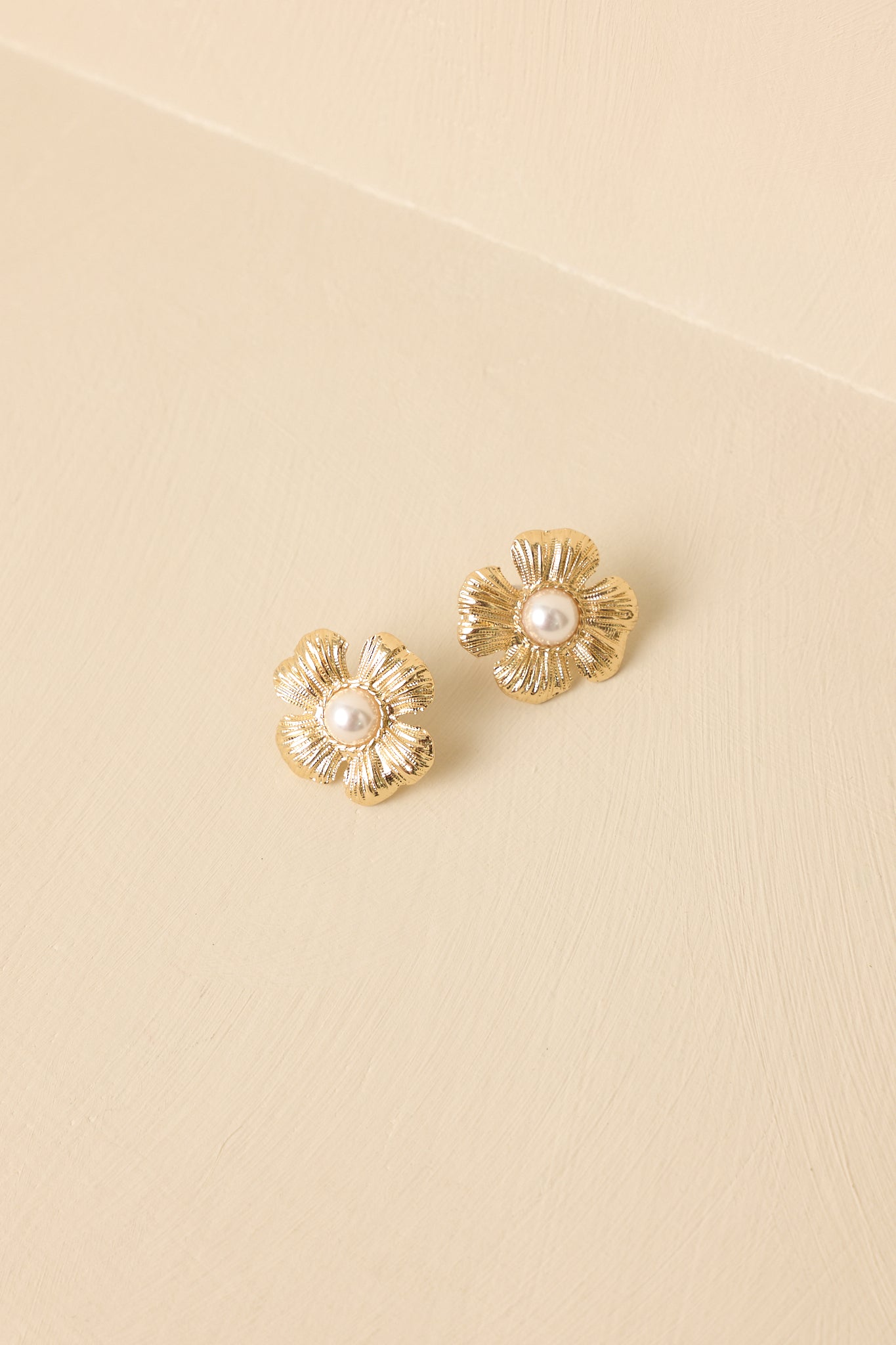 Detailed close-up of the gold-tone earrings focusing on the textured petals and pearl-inspired centerpiece of the flower design.