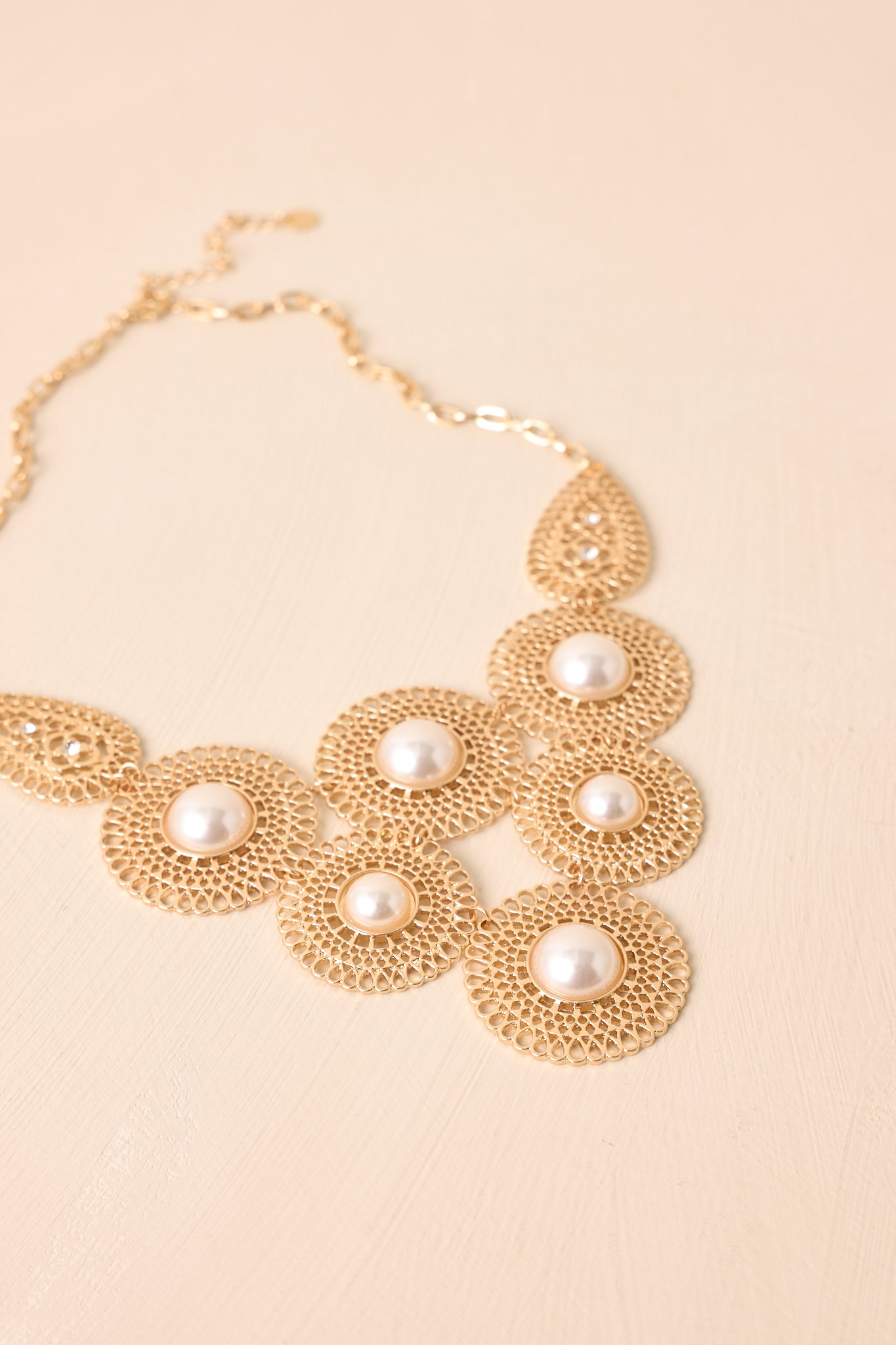 Close-up of the necklace, highlighting the filigree discs, ivory faux pearls, teardrop rhinestone connectors, and gold chain clasp.