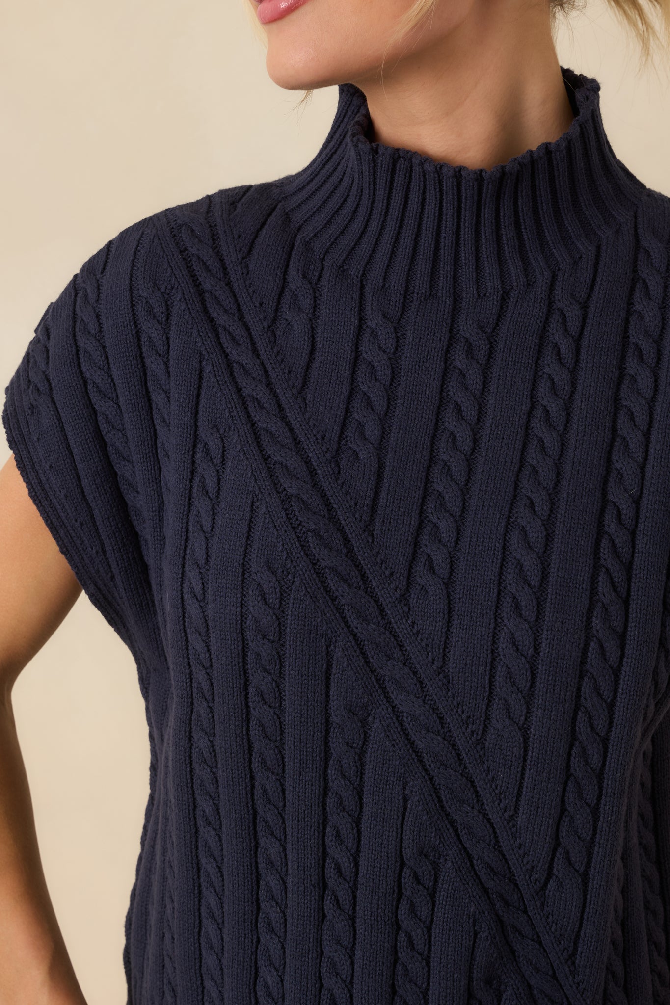 Close-up of the navy cable knit fabric highlighting the raised knit texture, ribbed trim, and clean stitch definition.