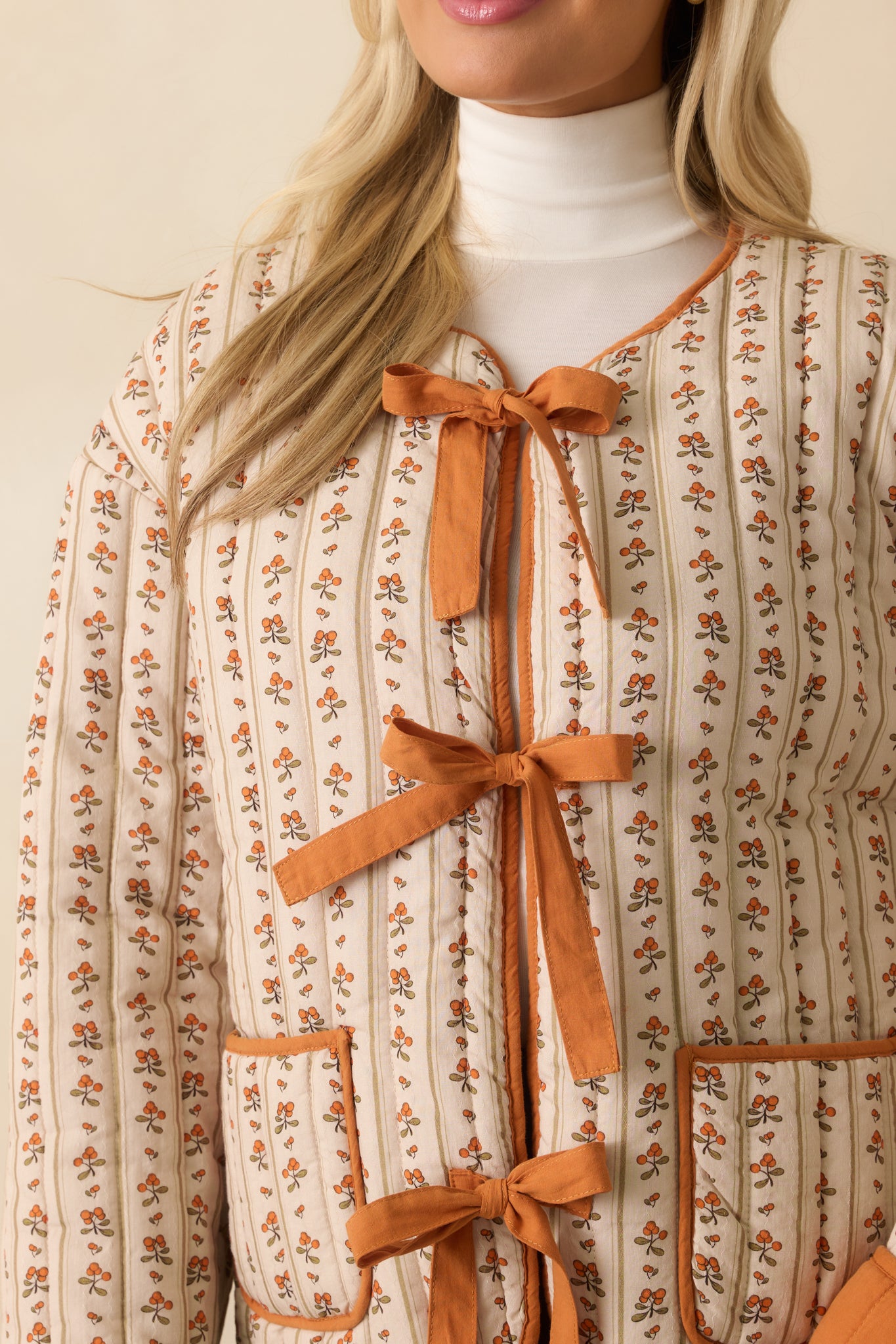 A close-up of the jacket fabric showing an ivory base, orange floral print, and quilted stitching with orange trim.