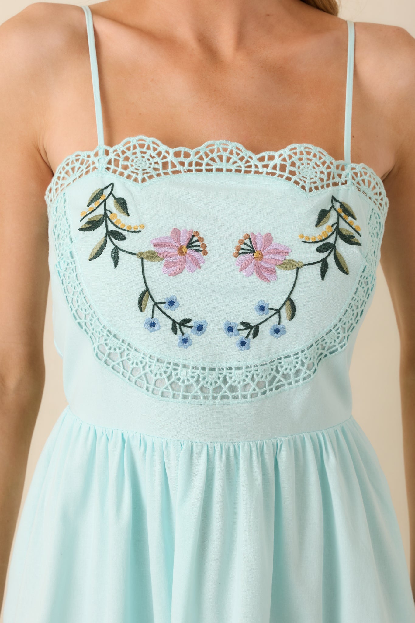 Close-up of ladder lace and embroidered flowers on light blue dress highlighting intricate stitching and texture.